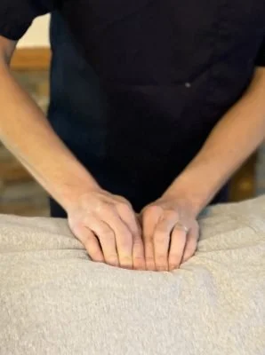 Person performing a massage on a beige fabric-covered surface.
