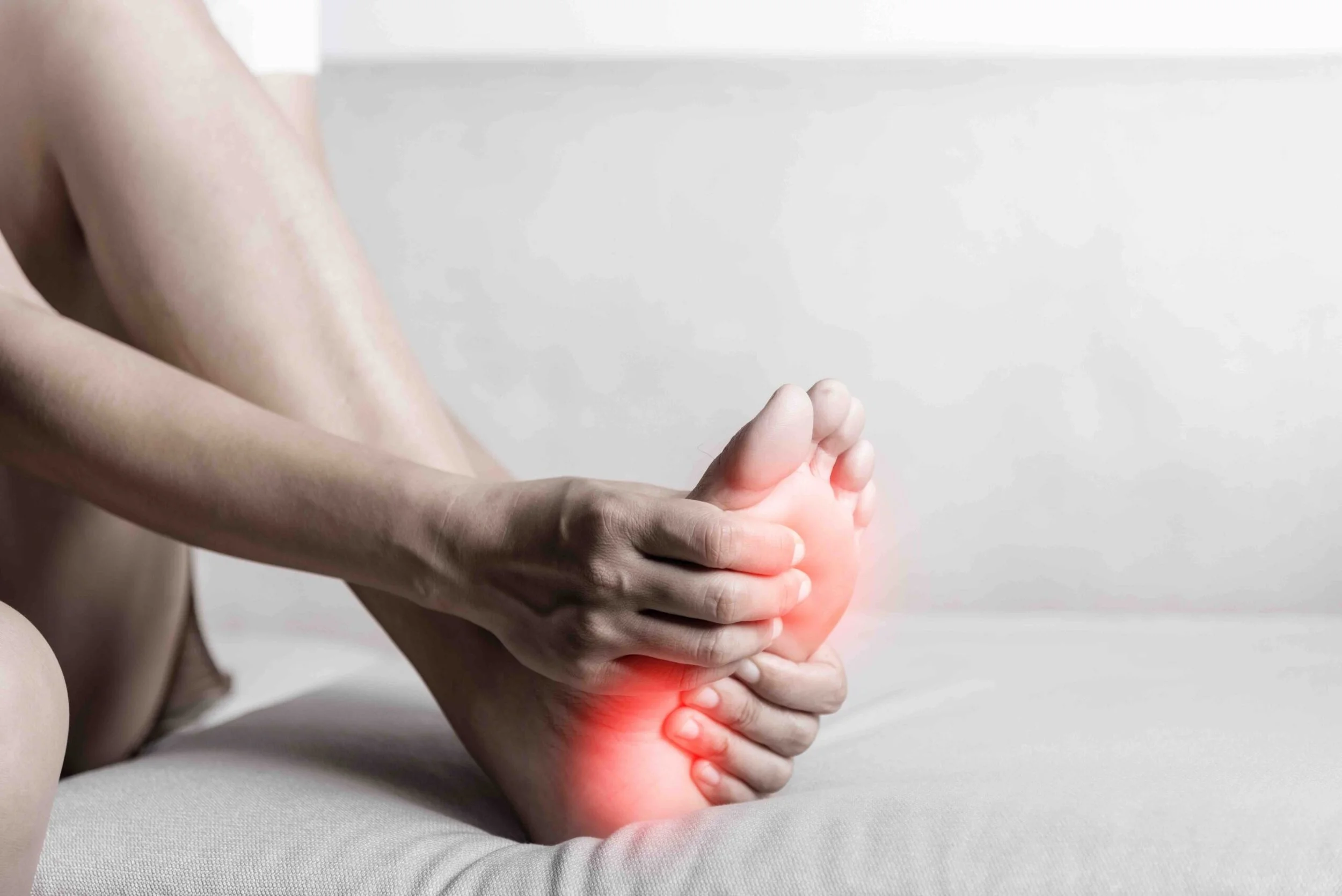 Person holding their foot with a red highlighted area indicating pain or injury.