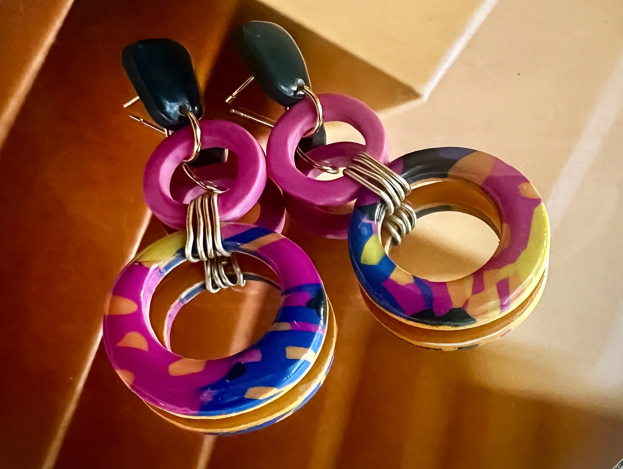 Colorful earrings with geometric shapes and bright patterns, resting on a wooden surface.