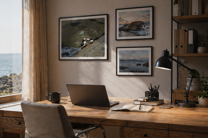 Bureau avec un ordinateur portable, une tasse, une lampe de bureau, des livres et des fournitures de bureau, avec des cadres photo de paysages de la mer accrochés au mur, près d'une fenêtre avec vue sur la mer.