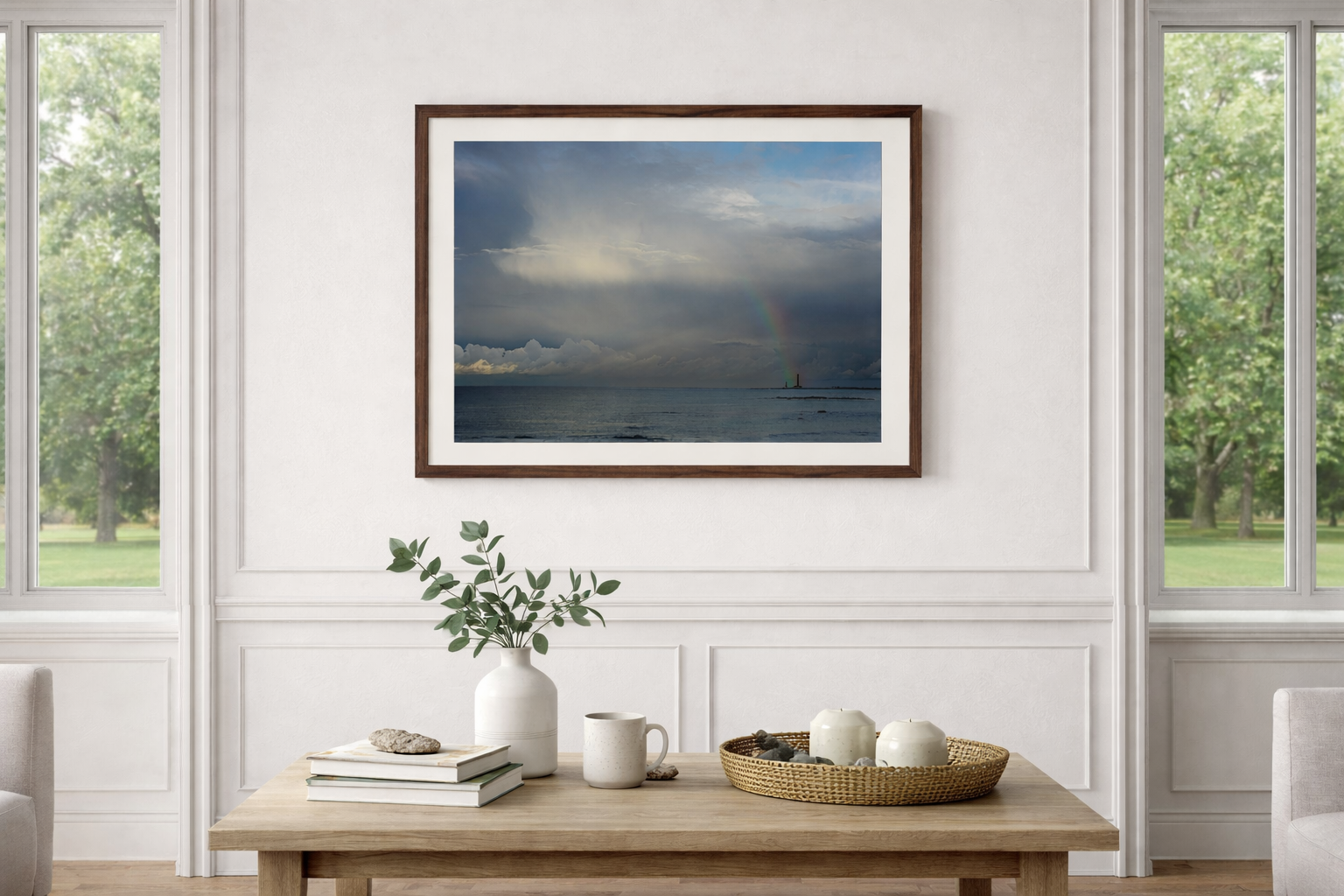 Une pièce lumineuse avec une grande fenêtre, un tableau représentant un paysage marin avec un arc-en-ciel, un vase avec des feuilles vertes, et divers objets décoratifs sur une table en bois.