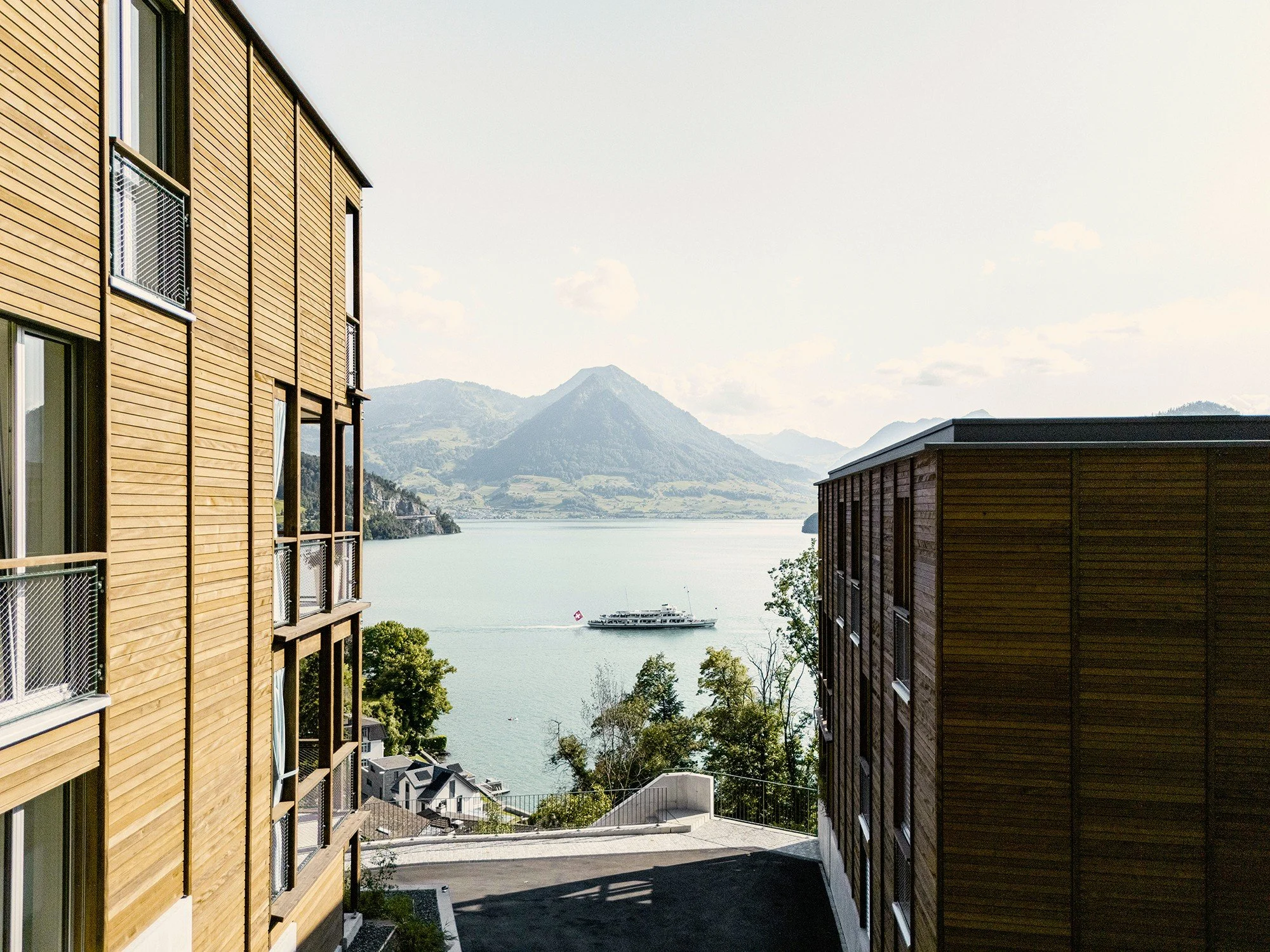 Blick auf einen See mit einer Yacht, umgeben von Bergen, zwischen zwei modernen Holzgebäuden.