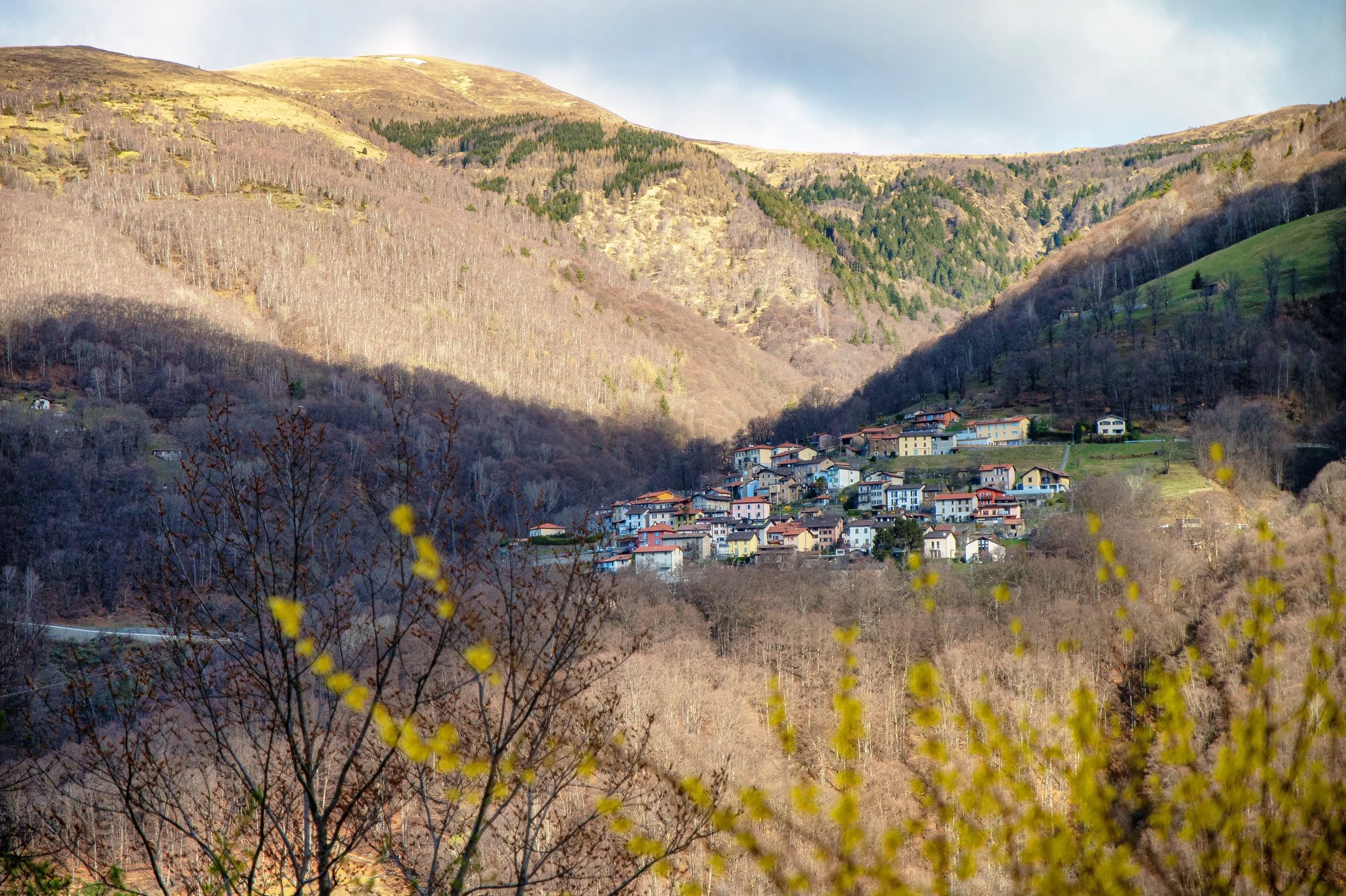 Häuser auf einem Hang inmitten eines gebirgigen, teilweise bewaldeten Geländes im Frühling.