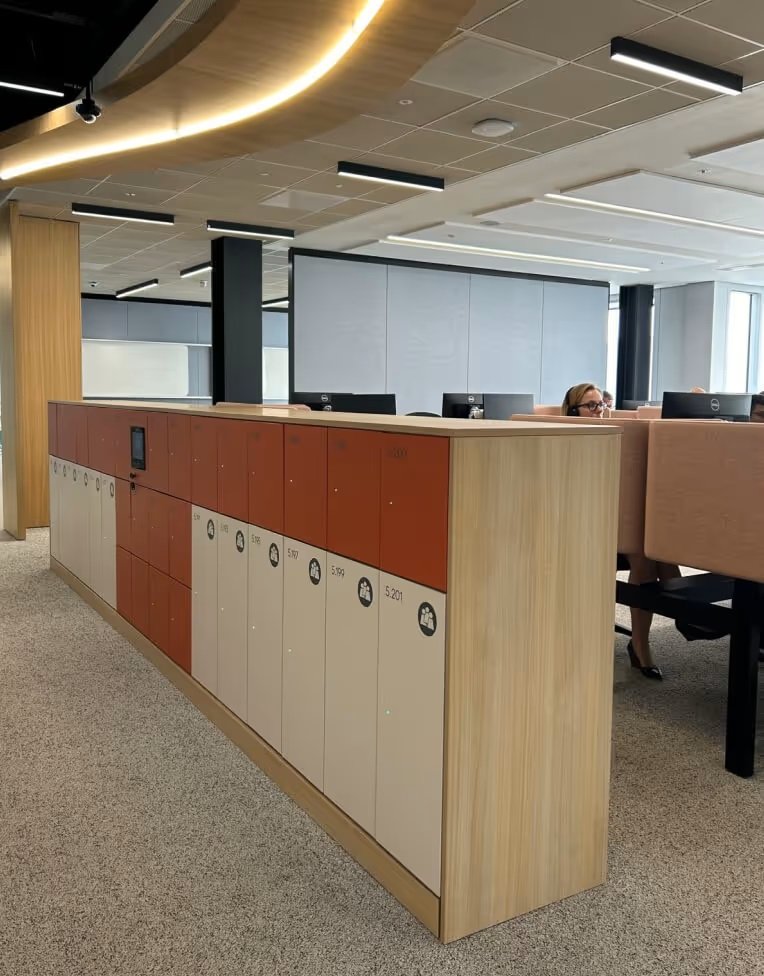 Office space with a wooden lockable storage unit, workstations, computers, and a patterned ceiling with black and gold lighting fixtures.