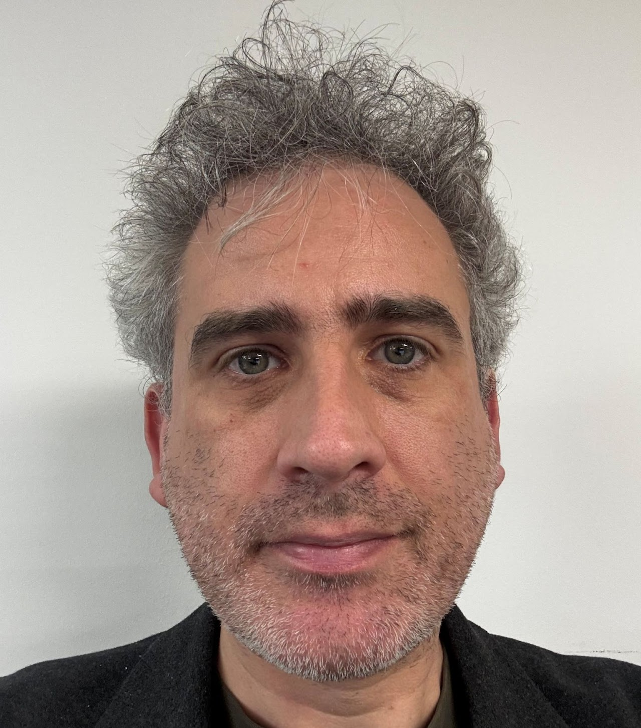 Close-up of a middle-aged man's face with gray, curly hair, blue eyes, and a slight beard, against a plain white background.