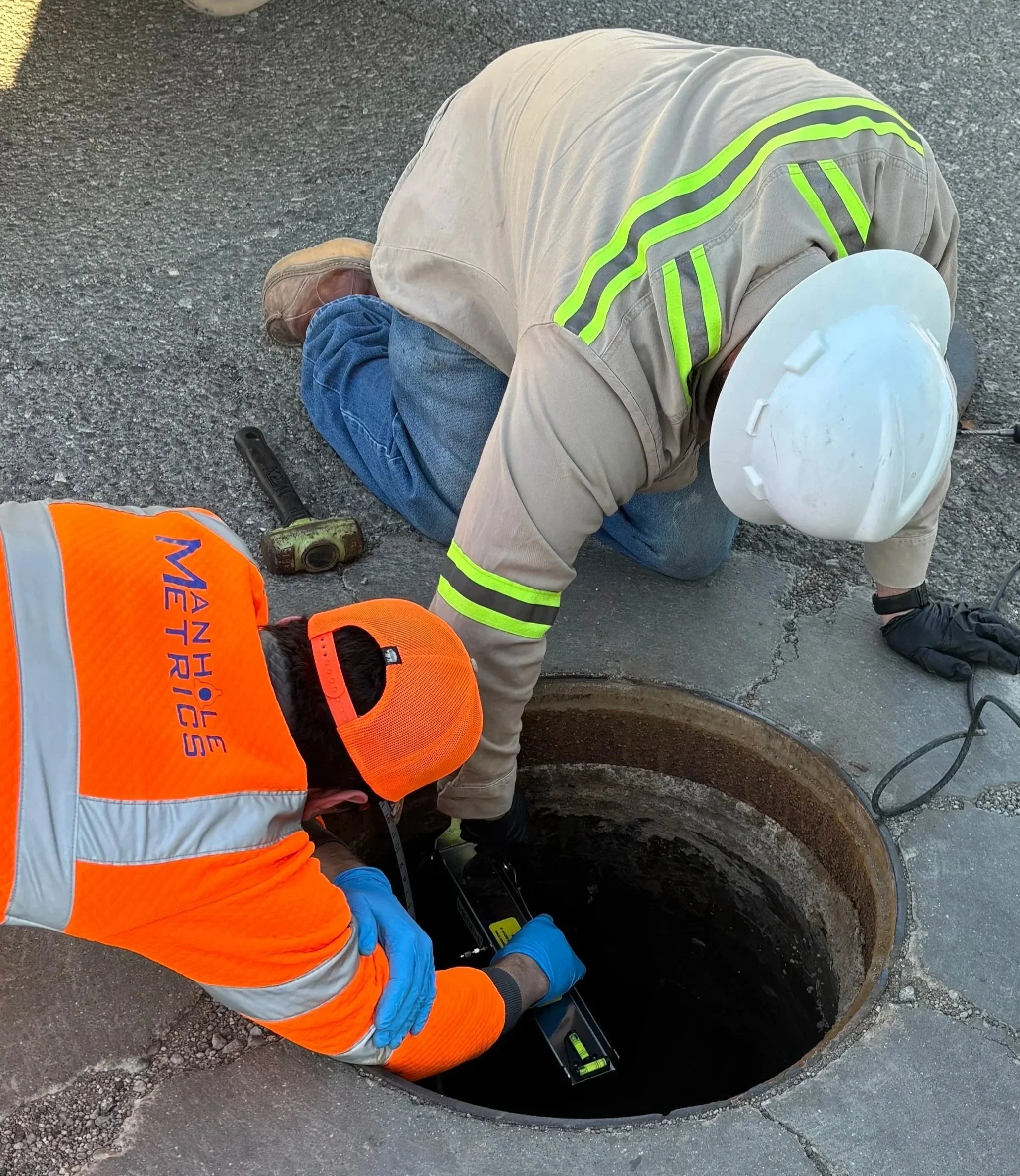 A construction worker installing sewer wastewater level sensor in a manhole, using a level to check the alignment of the pipe. The worker is installing ManholeMetrics technology