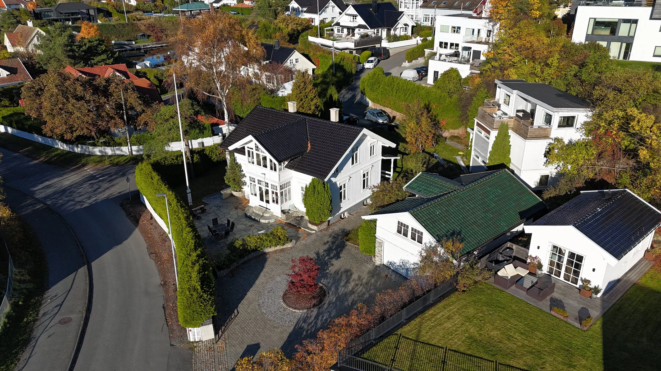Aerial view of a neighborhood with white houses, landscaped yards, trees with fall foliage, and a curved street.