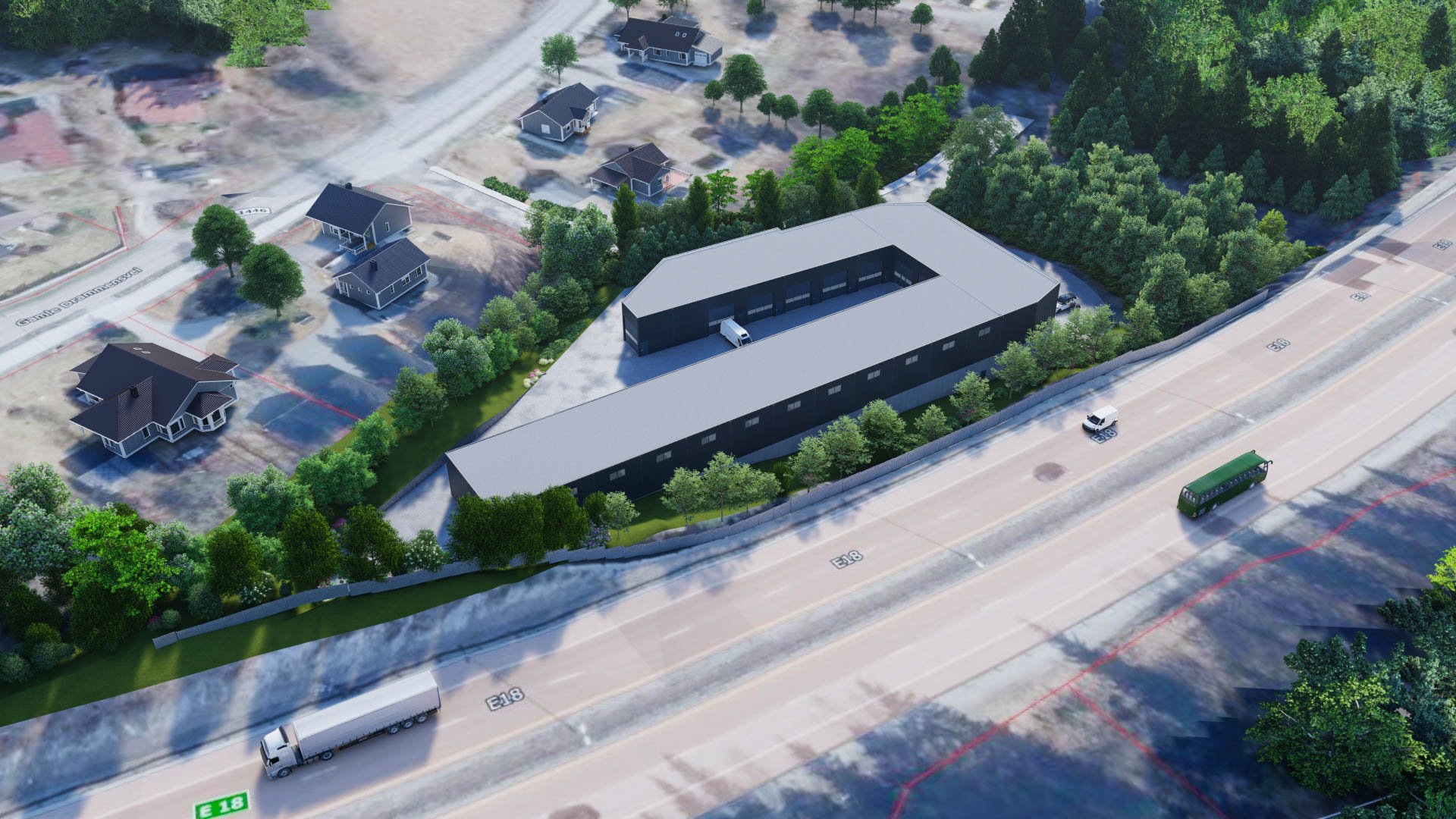 Aerial view of a large modern building with a U-shaped layout, surrounded by trees and a parking lot, next to a highway with vehicles passing by. Smaller houses and wooded areas are visible nearby.