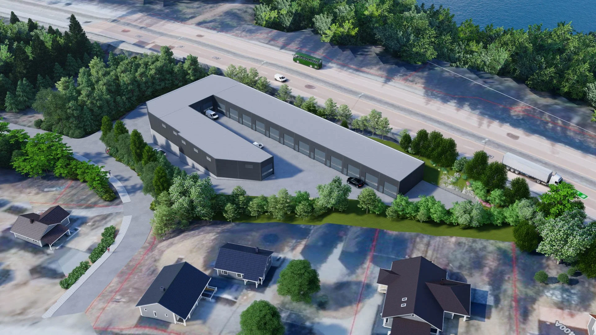 A modern rectangular building with a gray roof, surrounded by trees and a parking lot, situated near a road with cars, and a body of water in the background.