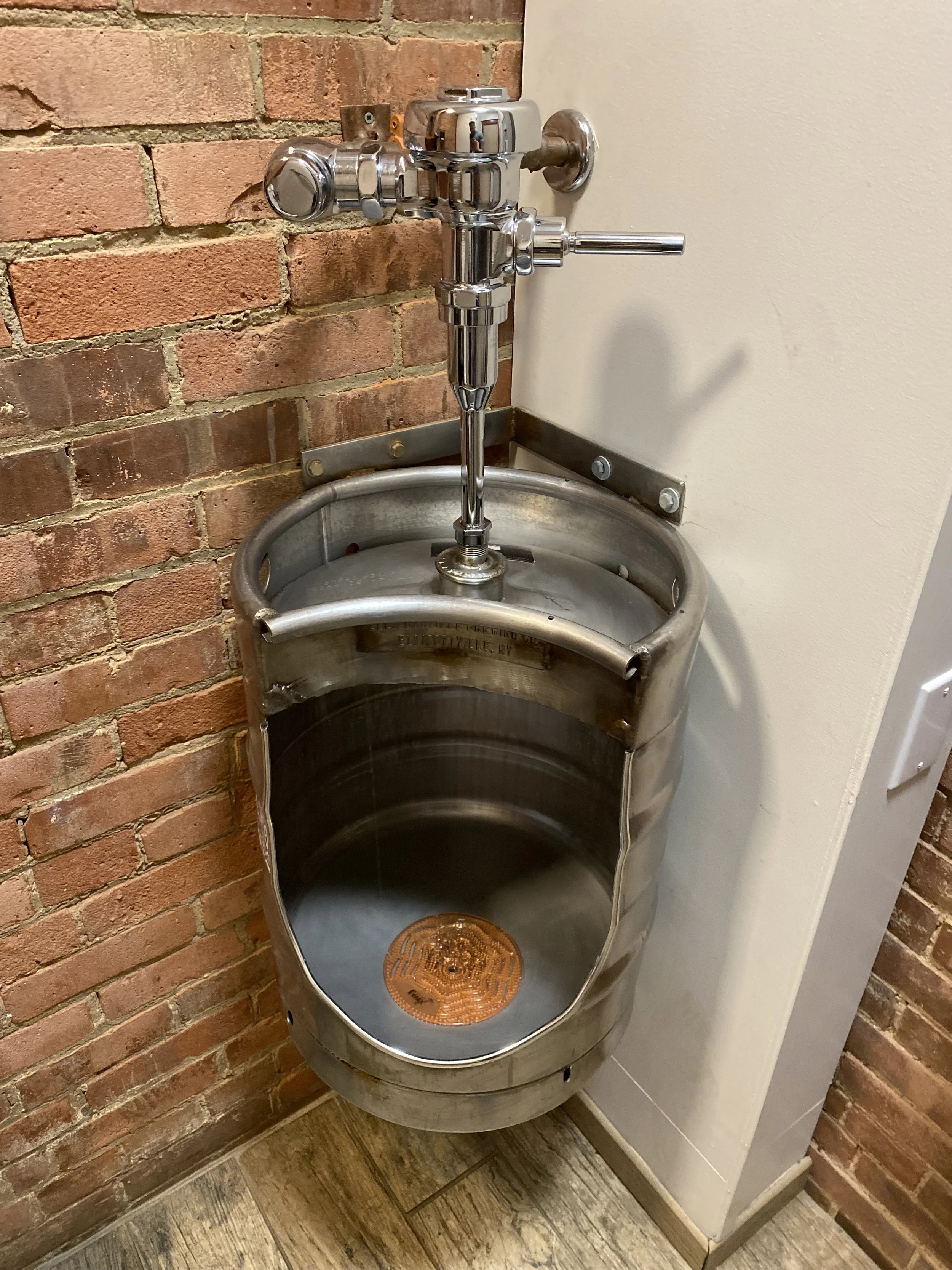 A stainless steel hand wash sink with a faucet, mounted on a brick wall, with a drain cover at the bottom.
