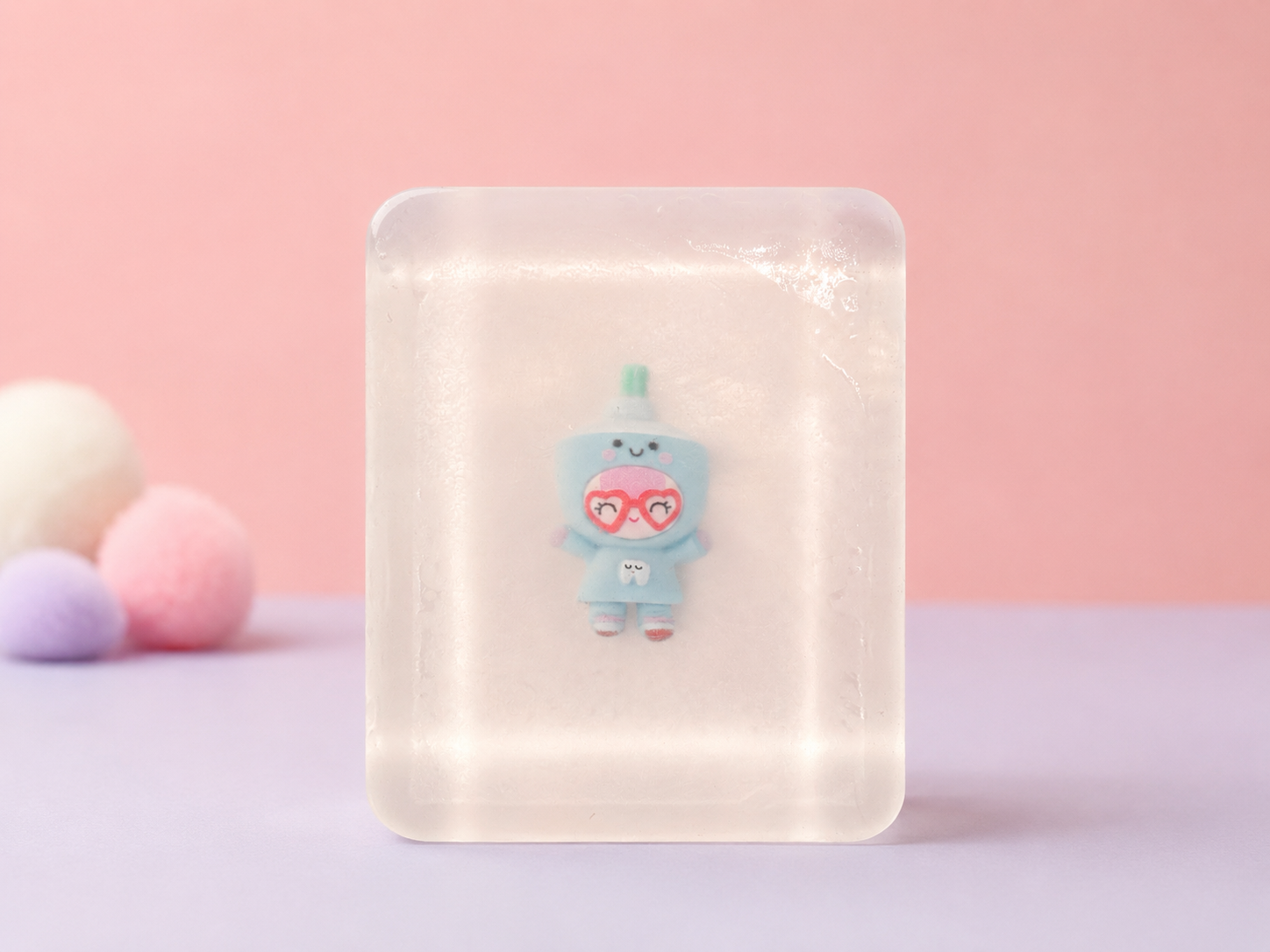 Transparent handmade soap with cute blue collectible figurine inside, with pastel pink background