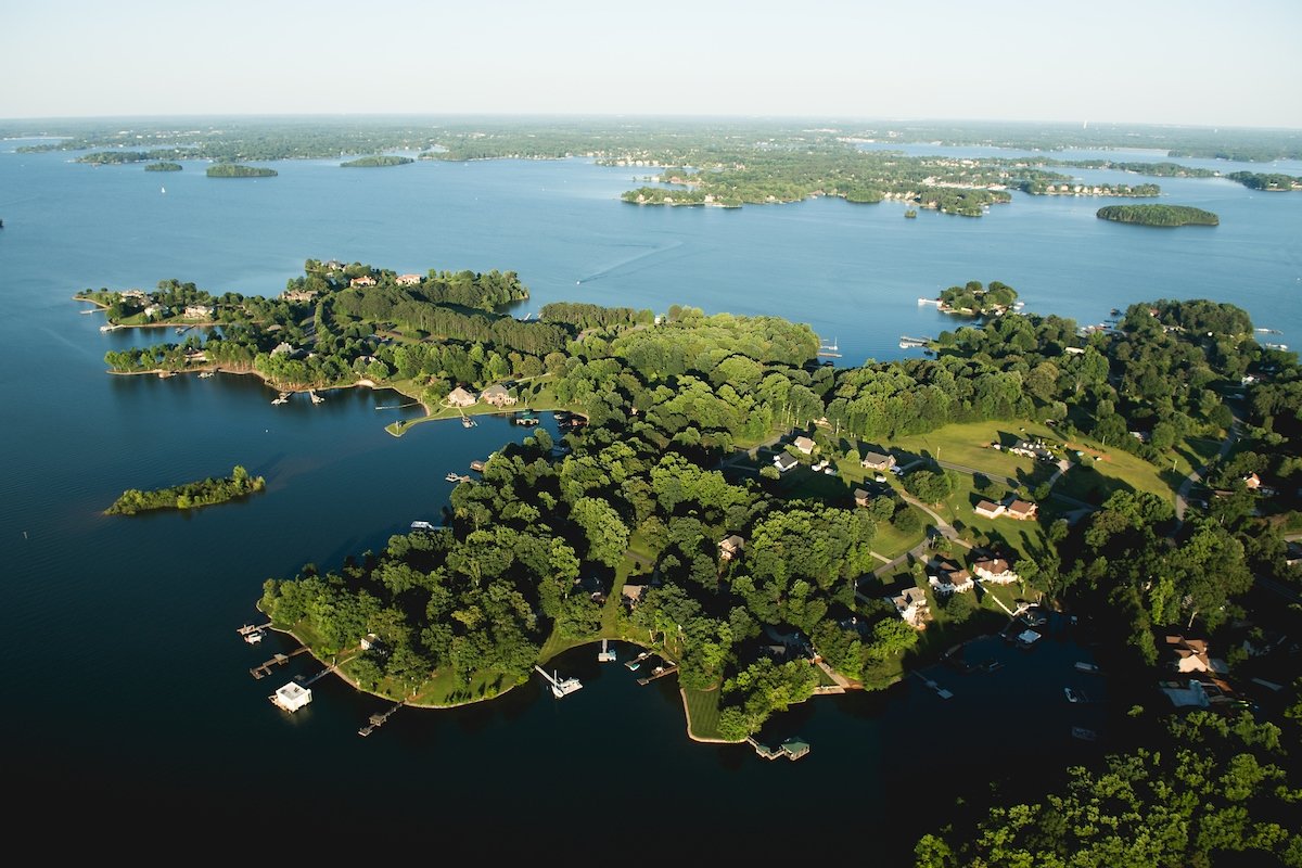Aerial view of a peninsula with residential homes surrounded by water and lush green trees, with boats docked along the shoreline and in the water.