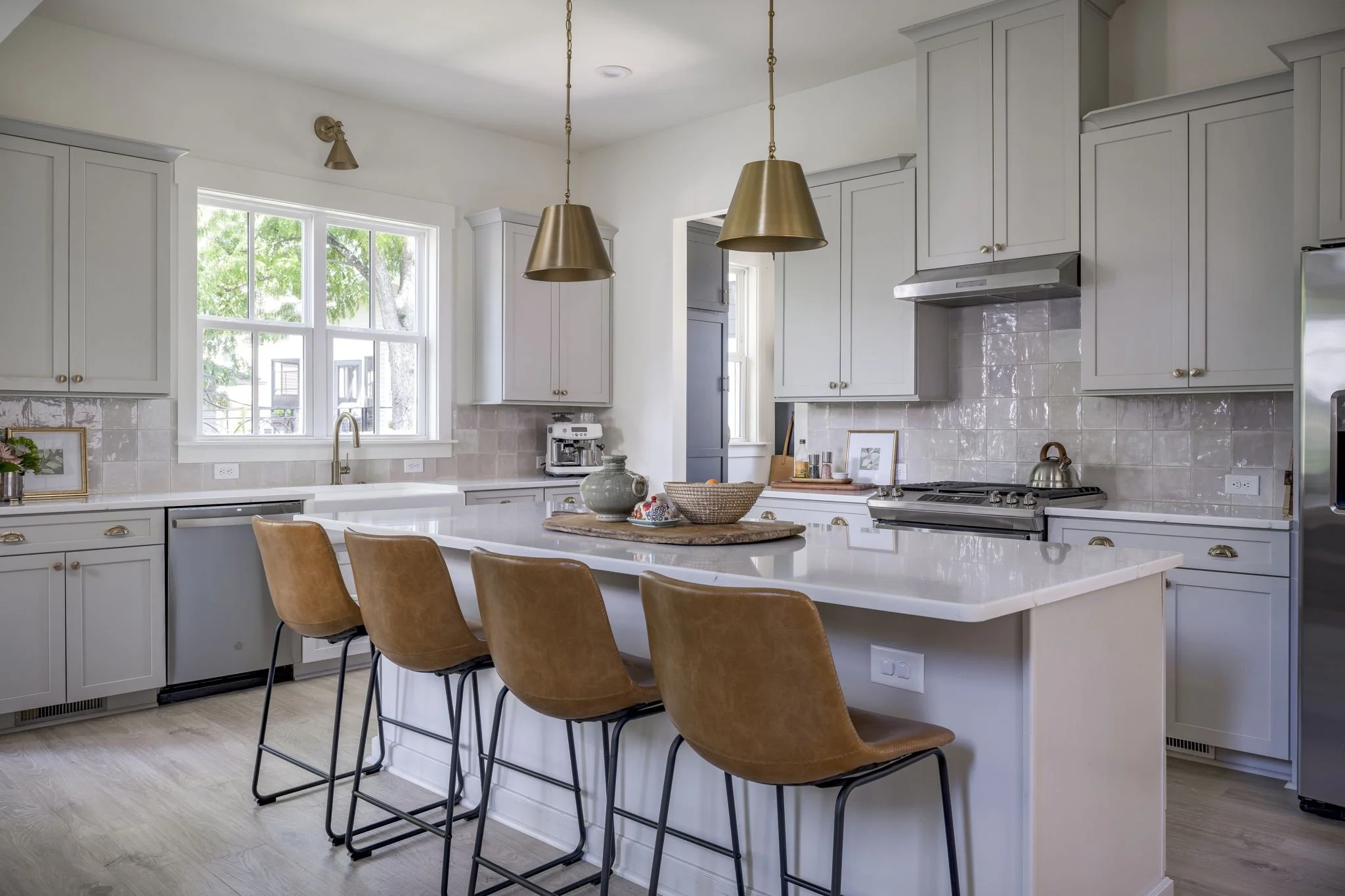 Modern kitchen with white cabinets, a central island with four brown bar stools, tile backsplash, stainless steel appliances, and pendant lighting.