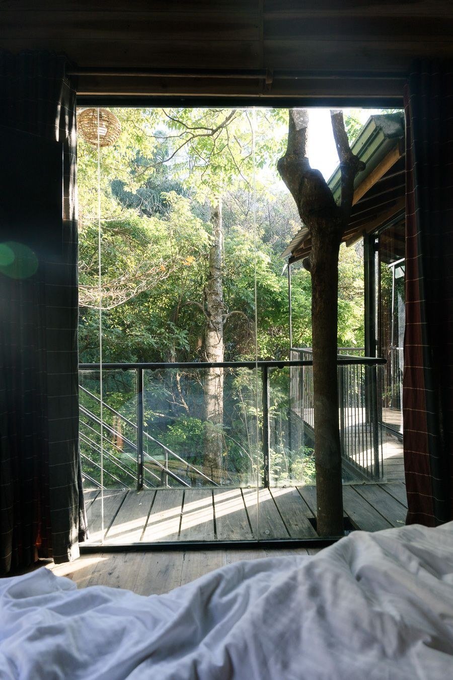 View from the bed through open doors onto the treehouse balcony and forest at The Glenrock, Sri Lanka