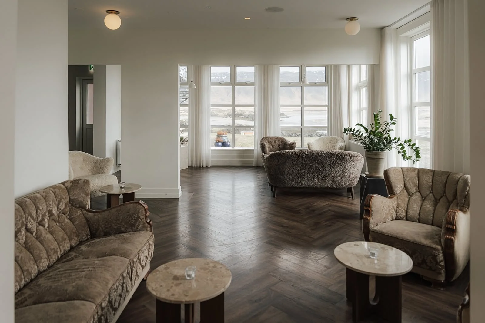 Bright lounge with velvet sofas, round tables and tall windows at Hótel Búðir, Iceland