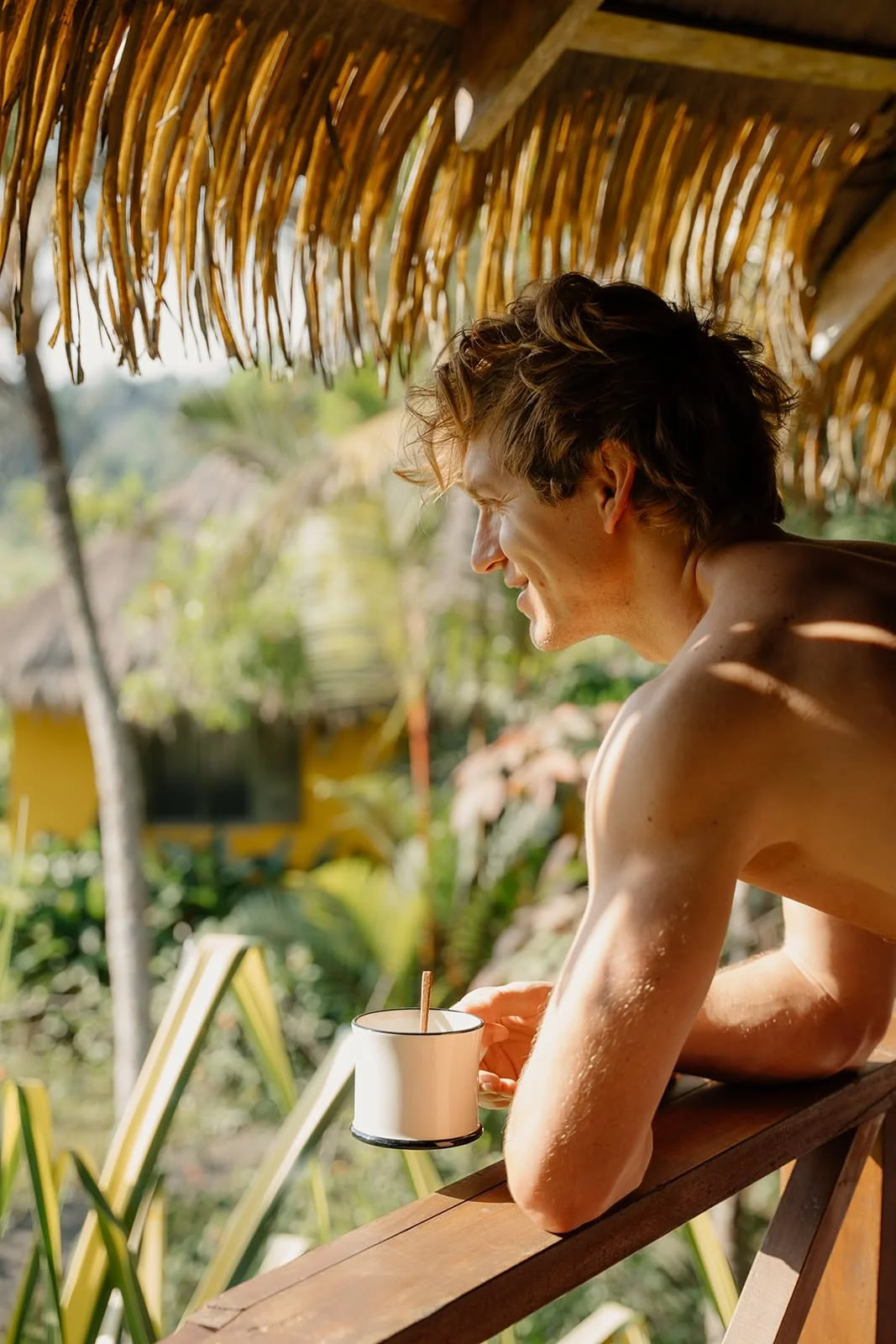 Man with a cup of coffee leaning on a wooden railing under the thatched roof at Huma Terra Lodge, Sri Lanka