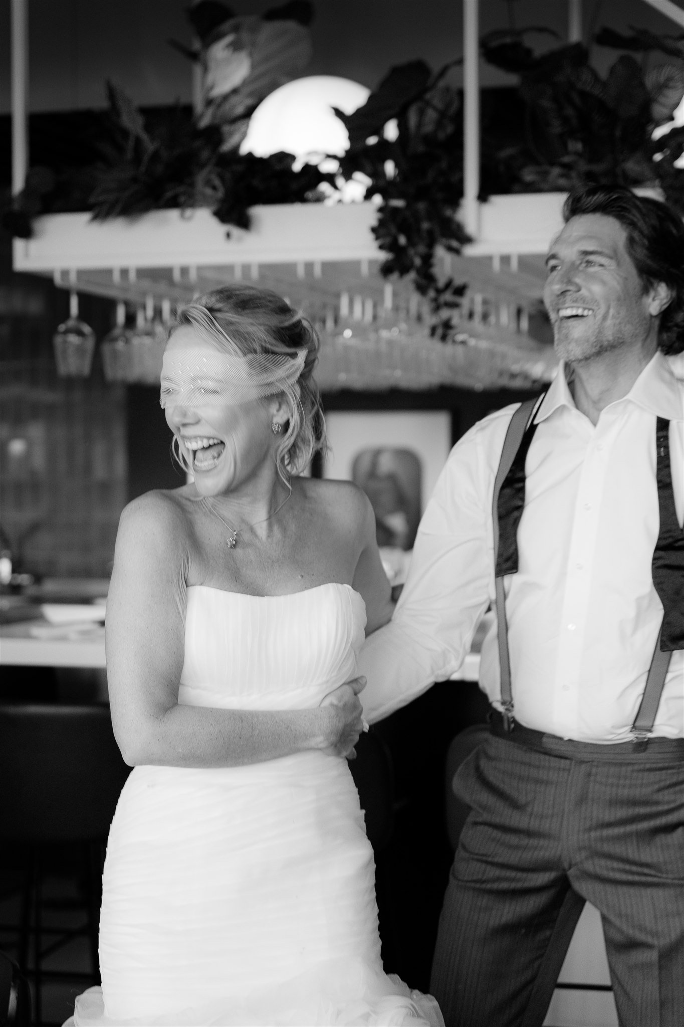 In diesem schwarz-weißen Bild lachen eine Frau in einem Hochzeitskleid und ein Mann in formeller Kleidung gemeinsam.