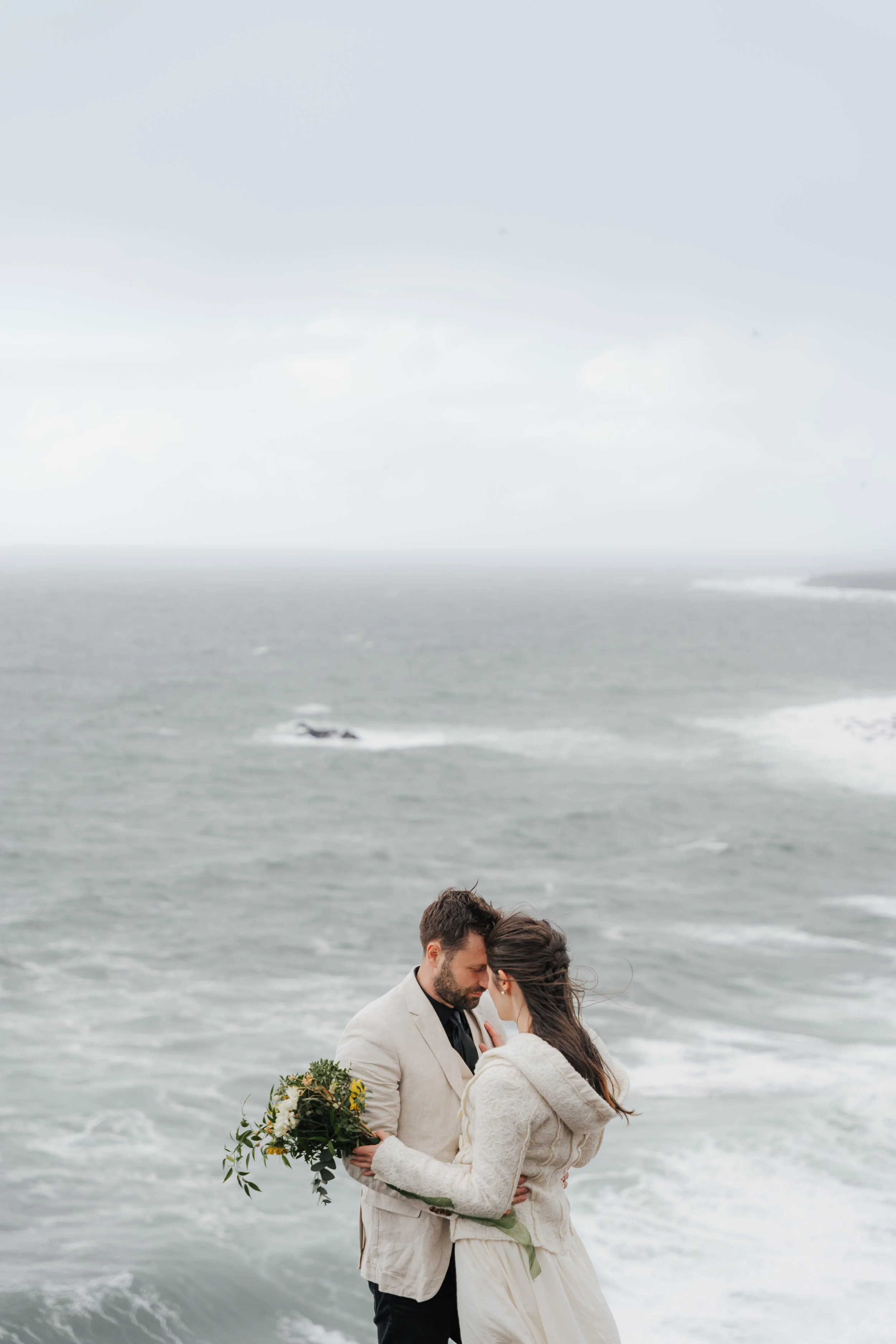 Ein verliebtes Paar, das am Strand nahe dem Wasser steht, sich küsst und einander umarmt, während der Himmel bewölkt ist.