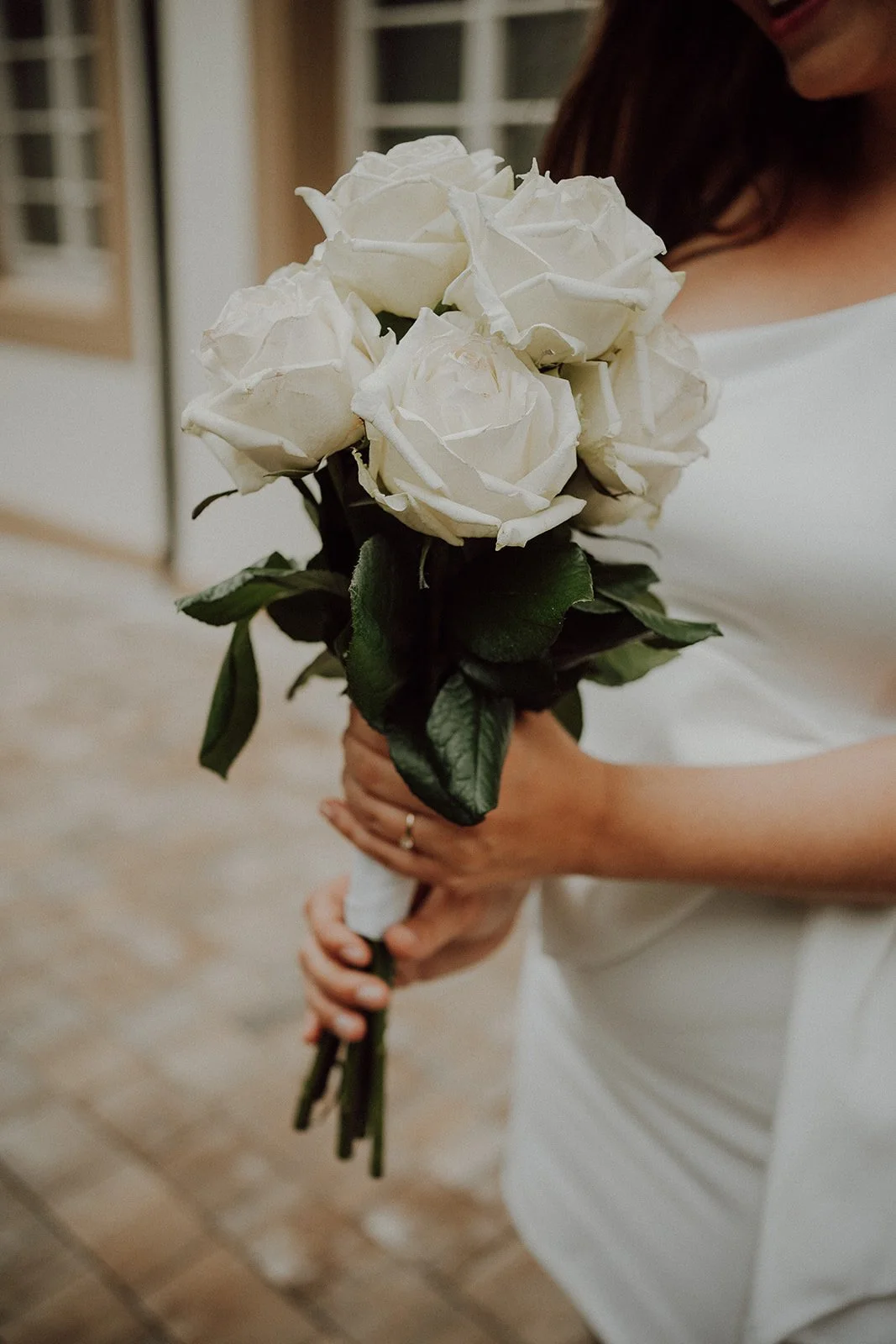 Frau in Weiß hält einen Strauß aus weißen Rosen bei einer Hochzeit.