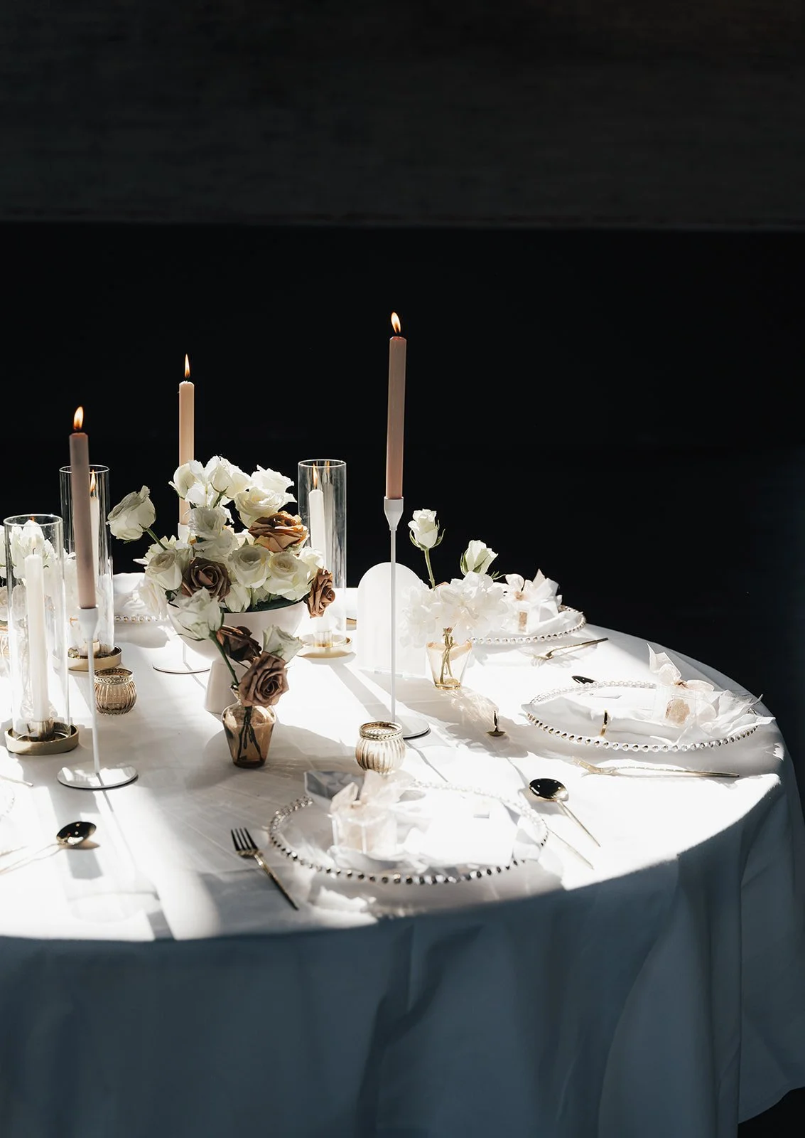 Eleganter festlicher Tisch mit weißen Blumen, Kerzen, Silberbesteck und edlem Geschirr auf weißer Tischdecke, stilvolle Dekoration.