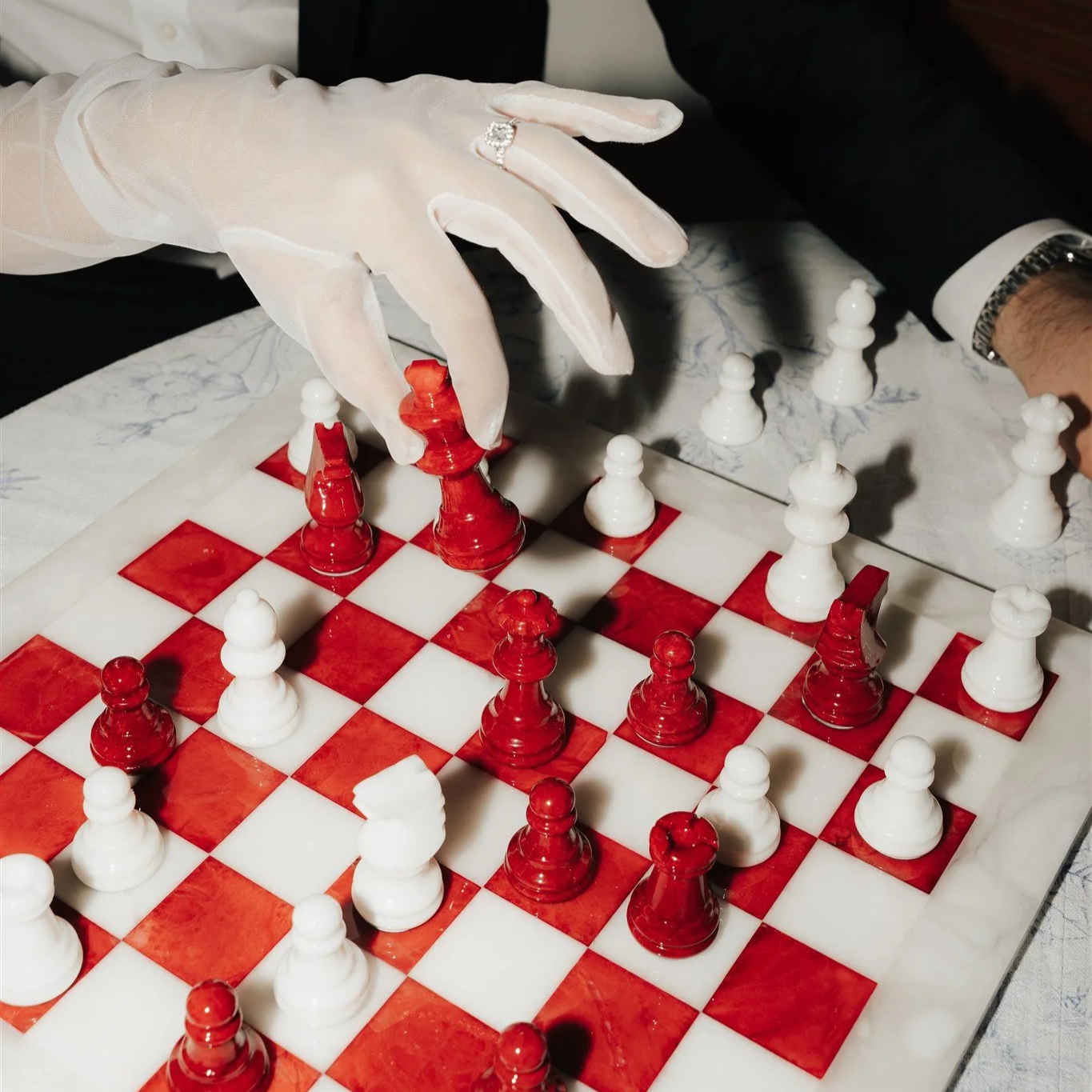 Editorial wedding cake concept inspired by chess symbolism. A fashion-forward wedding detail combining modern cake design, red and white chess pieces and elegant gloves. Contemporary editorial wedding photography capturing artistic bridal inspiration