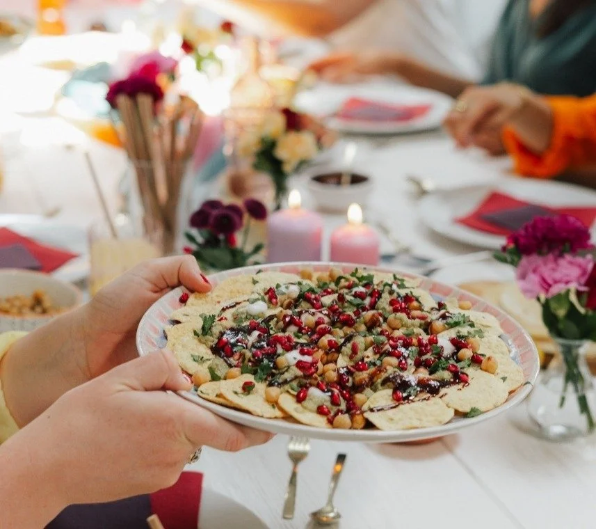 Hands passing a vegan sharing plate with pomegranate and herbs across a festive dinner table, from Plantiful Cooking