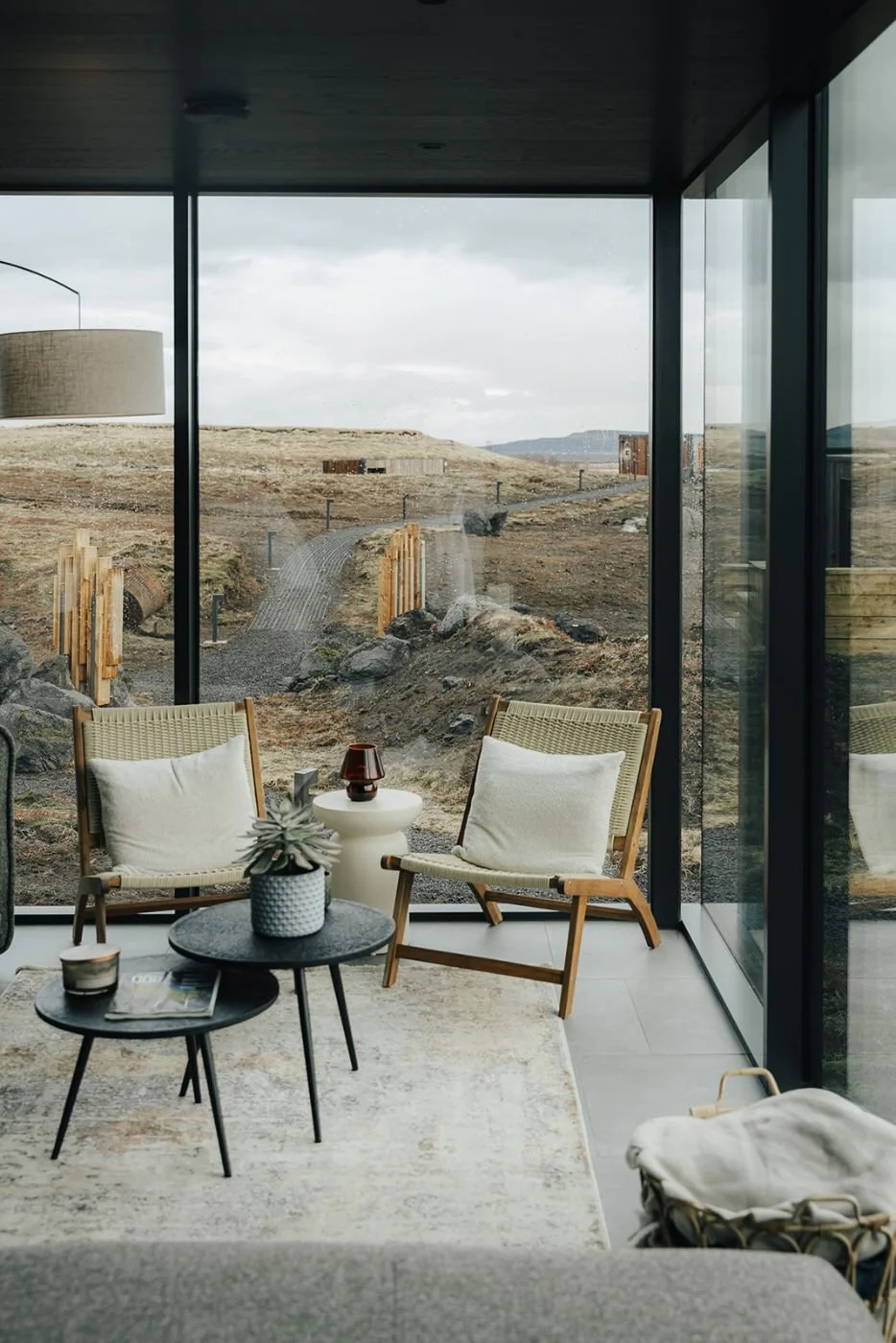 Lounge corner with woven armchairs inside a glass suite at ÖÖD Hekla Horizon, overlooking the Icelandic landscape