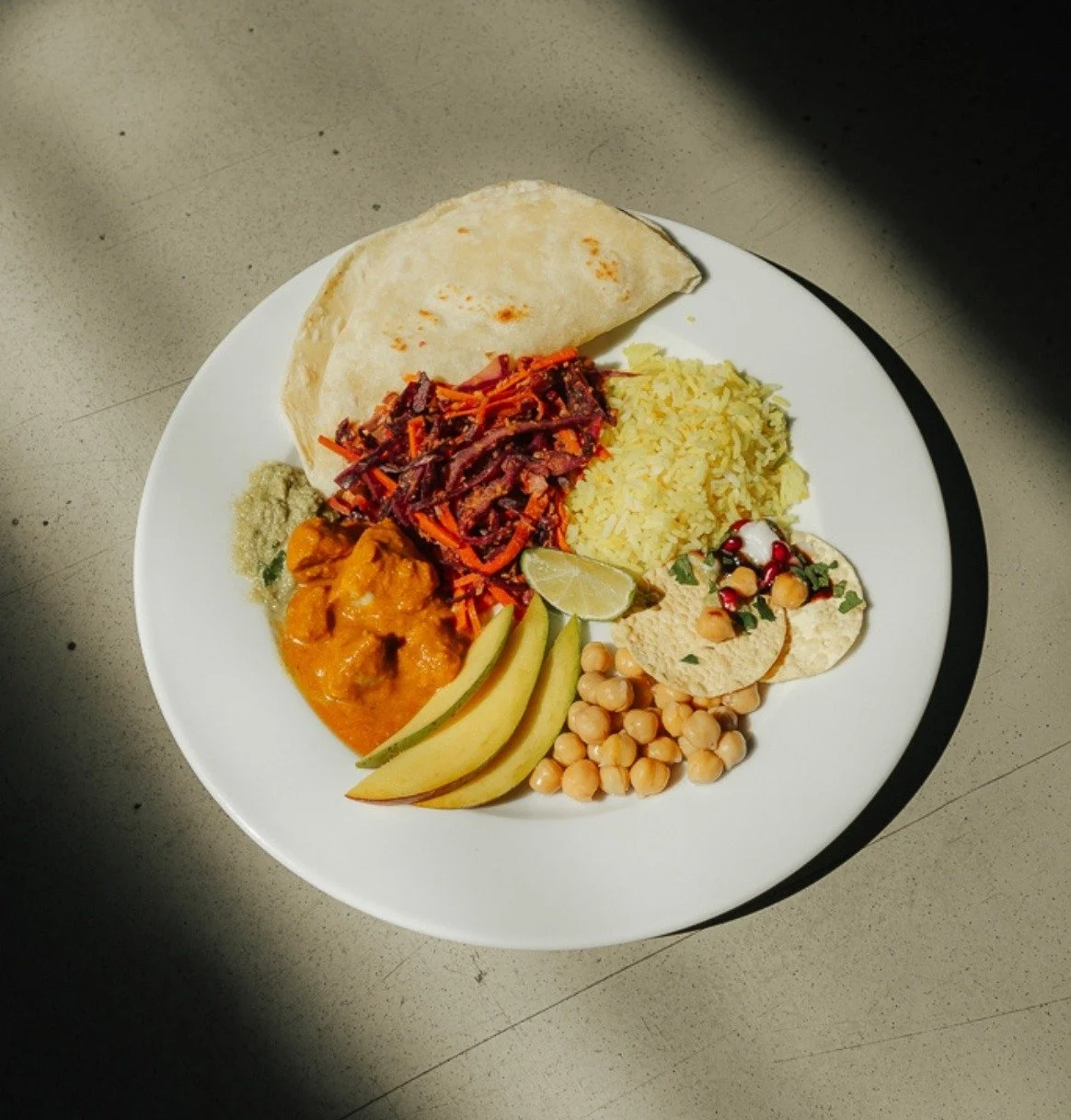 Colourful vegan plate with chickpeas, mango, flatbread and red cabbage in soft window light, from Plantiful Cooking