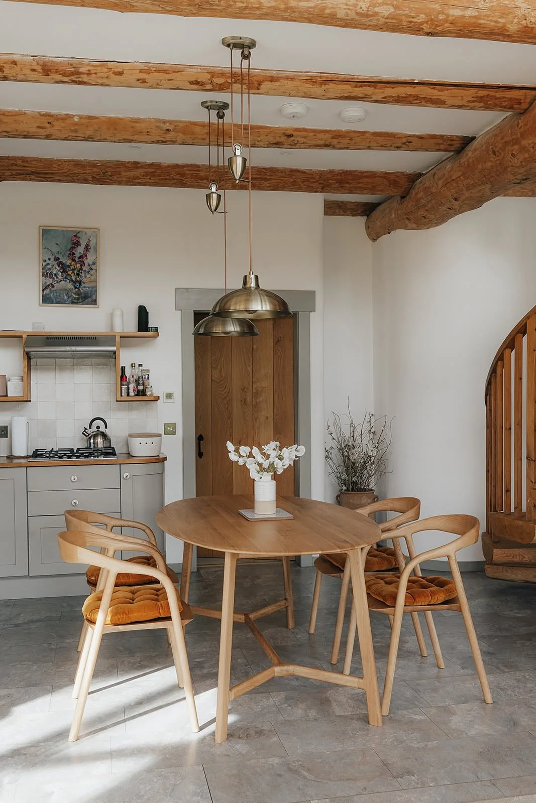 Round wooden breakfast table with chairs beneath timber beams in a bright cottage kitchen at Dunalastair, Scotland