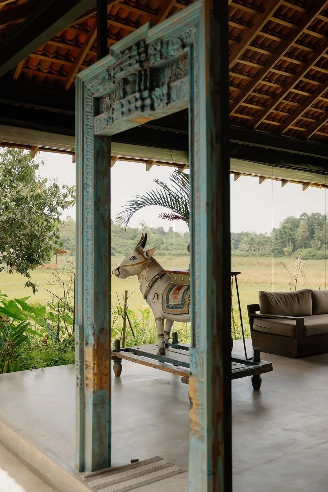 Weathered carved wooden doorway framing rice fields at Huma Terra Lodge, Sri Lanka – hotel photography by Anna van der Veen