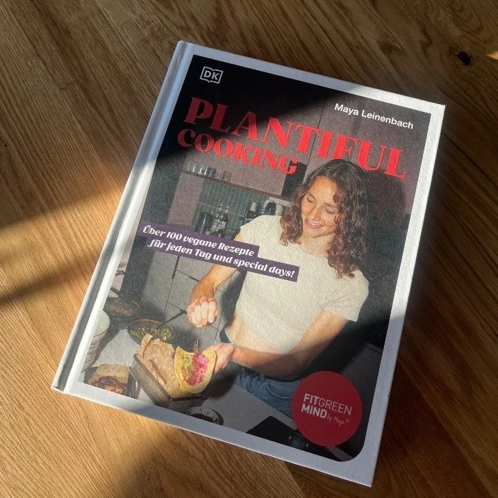 The printed Plantiful Cooking cookbook by Maya Leinenbach (Fitgreenmind), DK Verlag, on a sunlit wooden table