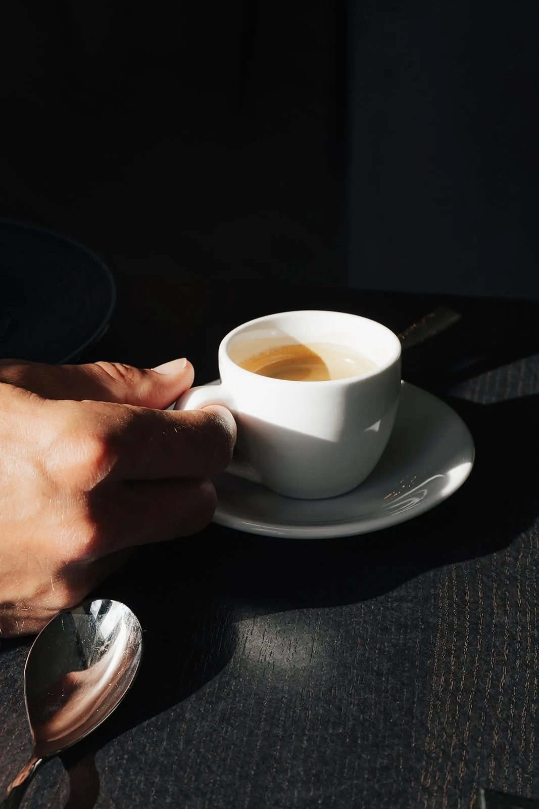 Hand holding a white espresso cup and saucer against a dark table at Hótel Búðir, Iceland