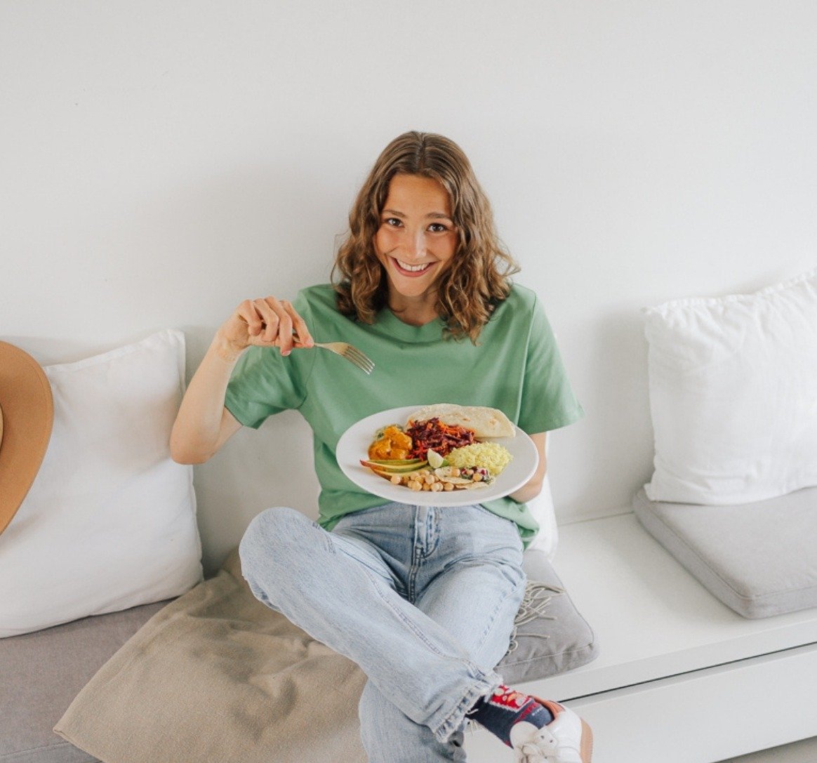 Maya Leinenbach smiling on a white bench with a plate of vegan food, from the Plantiful Cooking shoot