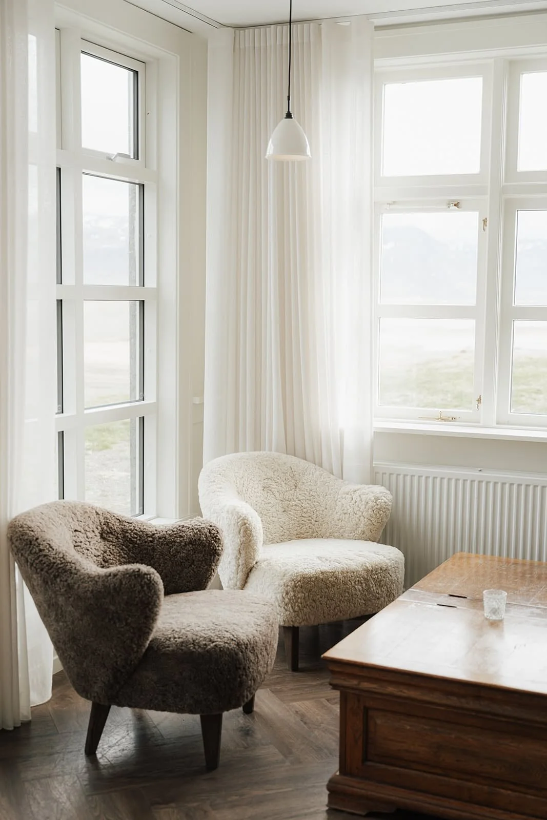 Two sheepskin armchairs beside tall white windows in a calm room at Hótel Búðir, Iceland