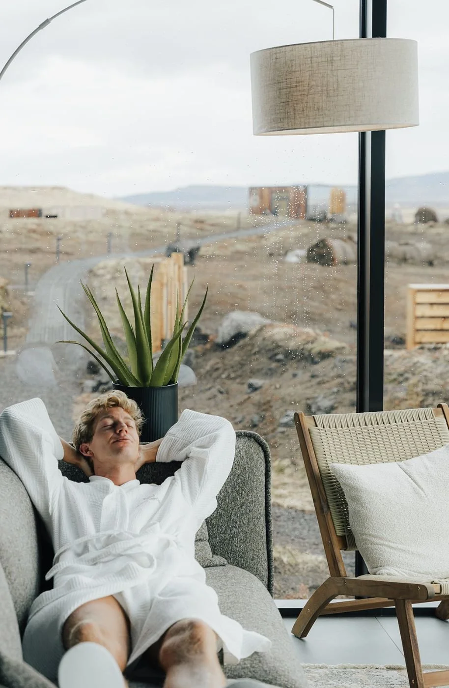 Guest in a white bathrobe relaxing in an armchair inside an ÖÖD Hekla Horizon mirror suite, Iceland