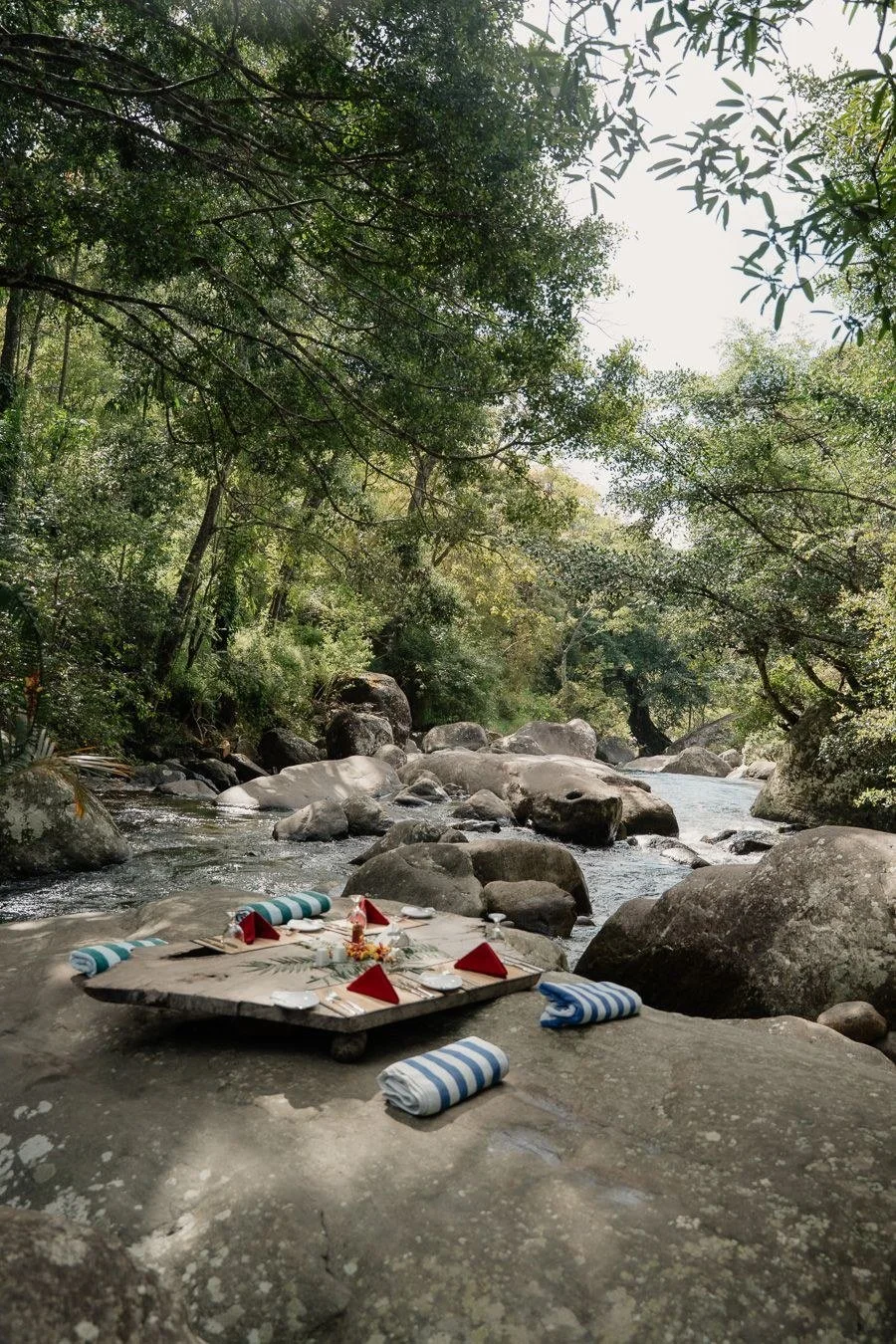 Breakfast set on a flat rock by the river with cushions and striped towels at The Glenrock, Sri Lanka