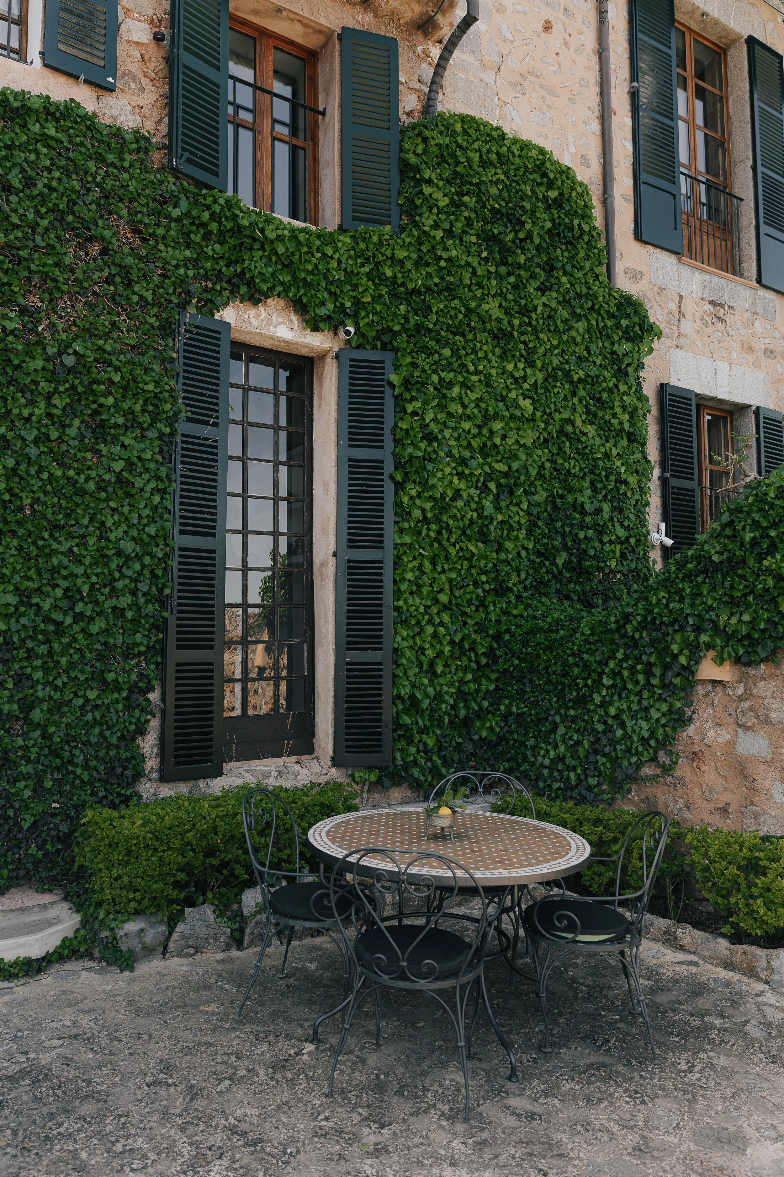 Ivy-covered stone façade with green shutters and a mosaic table on the terrace at Ca’s Xorc, Mallorca