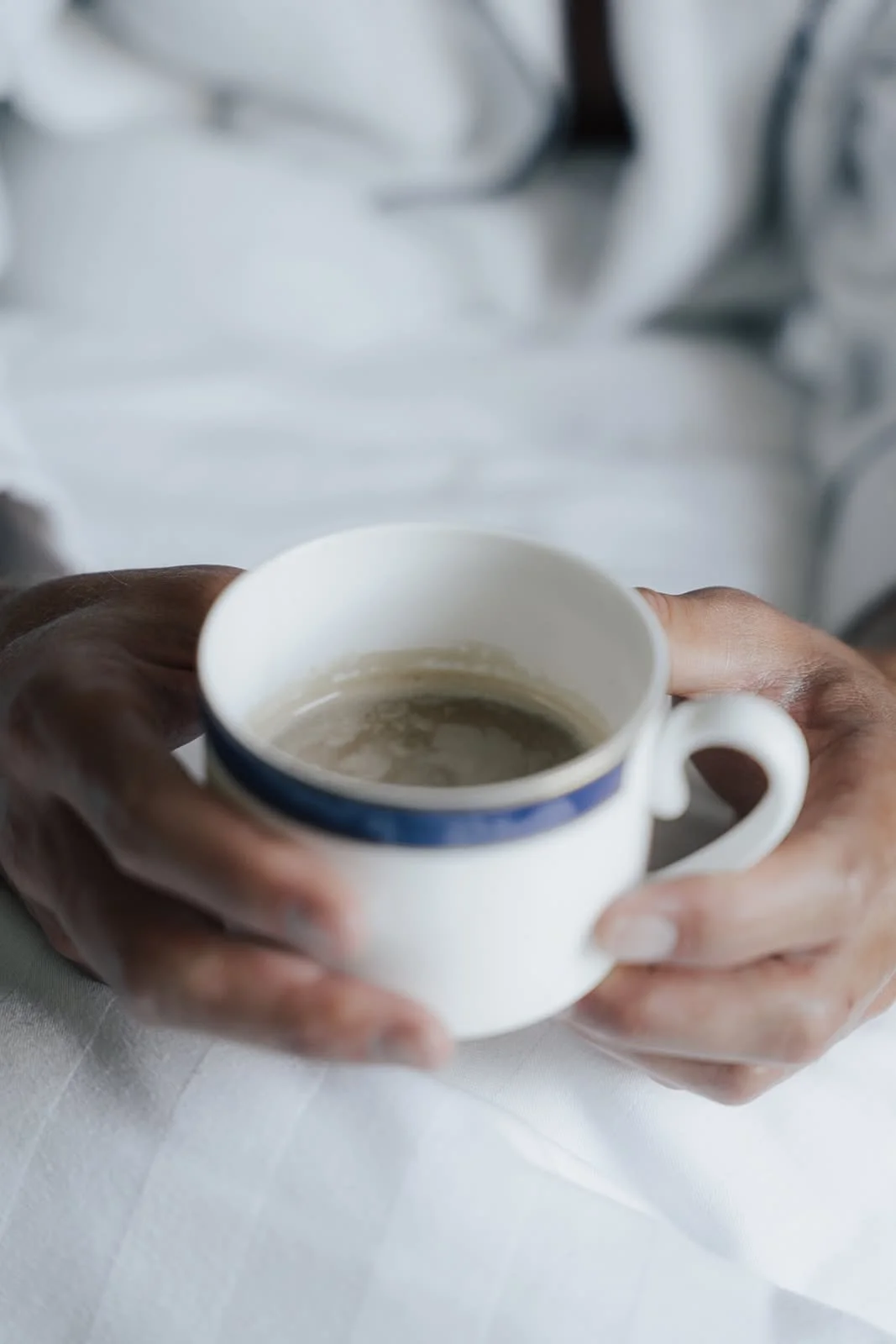 Hands holding a cup of coffee on white bed linen during a WILD Nurture retreat at Dunalastair, Scotland