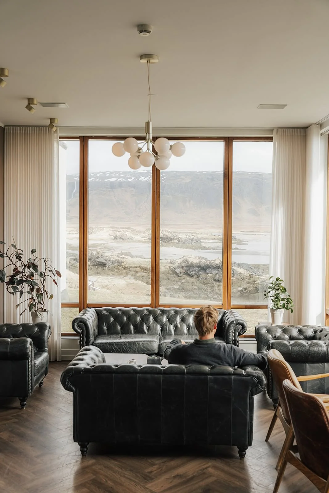 Guest relaxing on leather sofas in the lounge of Hótel Búðir, with tall windows facing the Icelandic coast