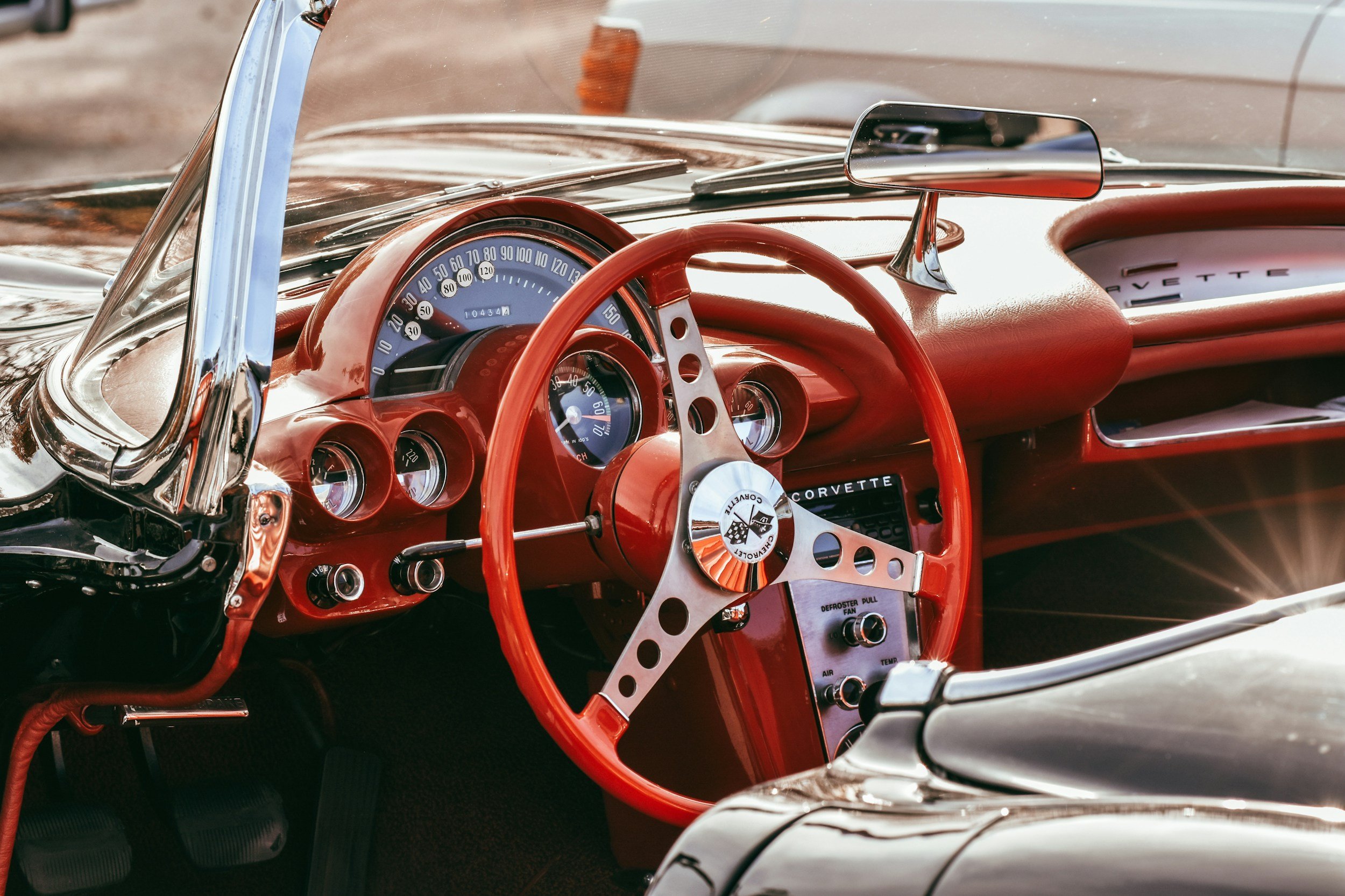Interior of a vintage red Corvette with a red steering wheel, classic gauges, and dashboard details.