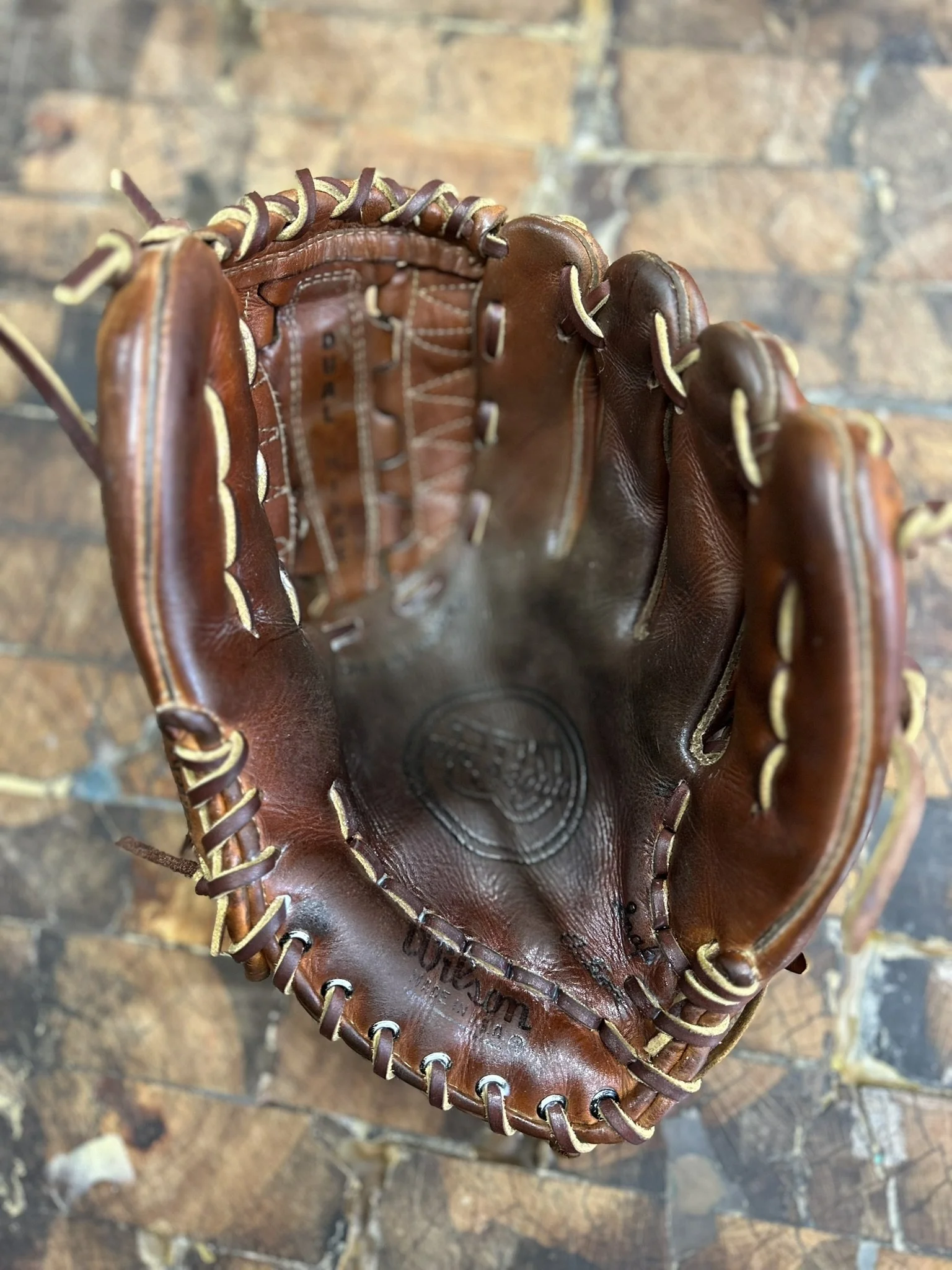 Inside view of a used brown leather baseball glove on a brick floor.