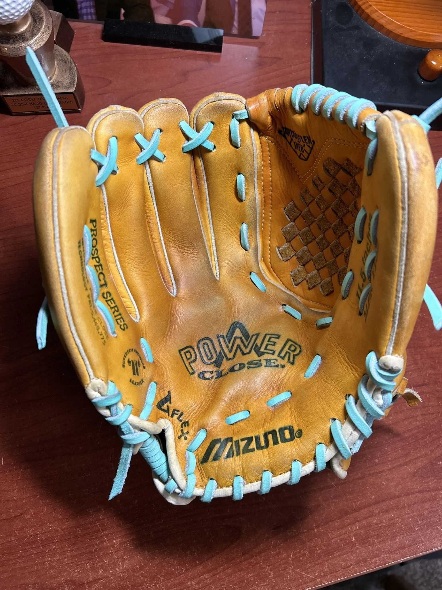 A yellow baseball glove with light blue laces, featuring brand logos Mizuno and others, placed on a wooden surface.