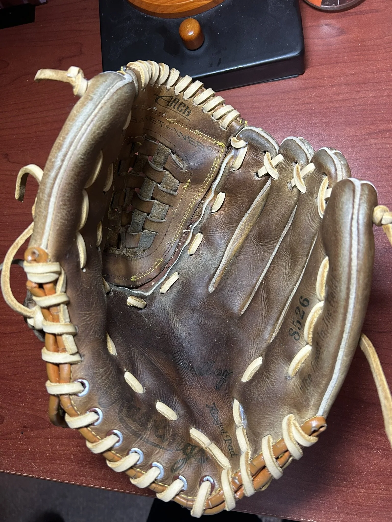 A vintage Wilson baseball mitt, brown leather with cream-colored lacing, placed on a reddish-brown wooden surface.