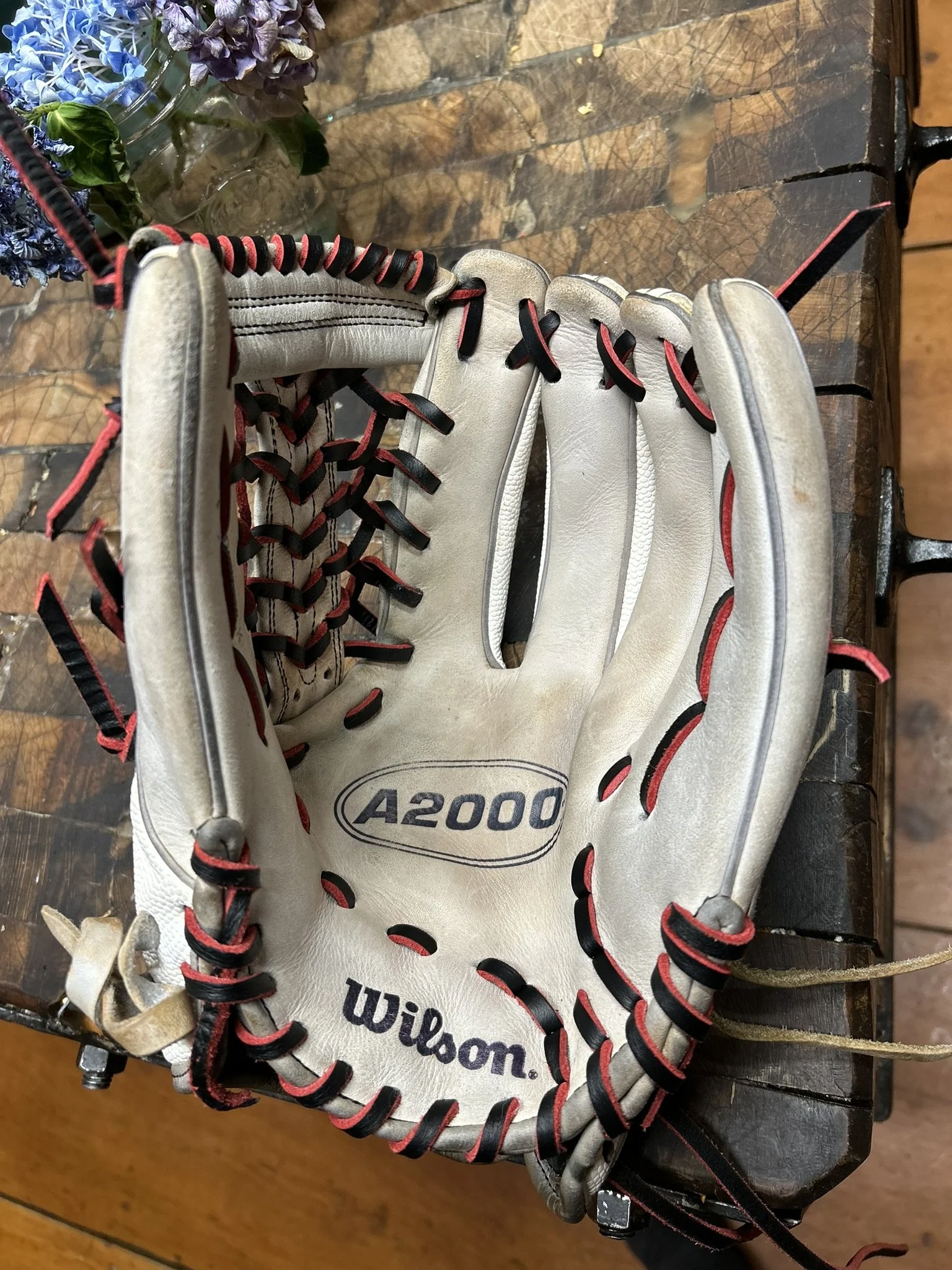 Worn Wilson A2000 baseball glove with black and red laces, placed on a wooden surface.