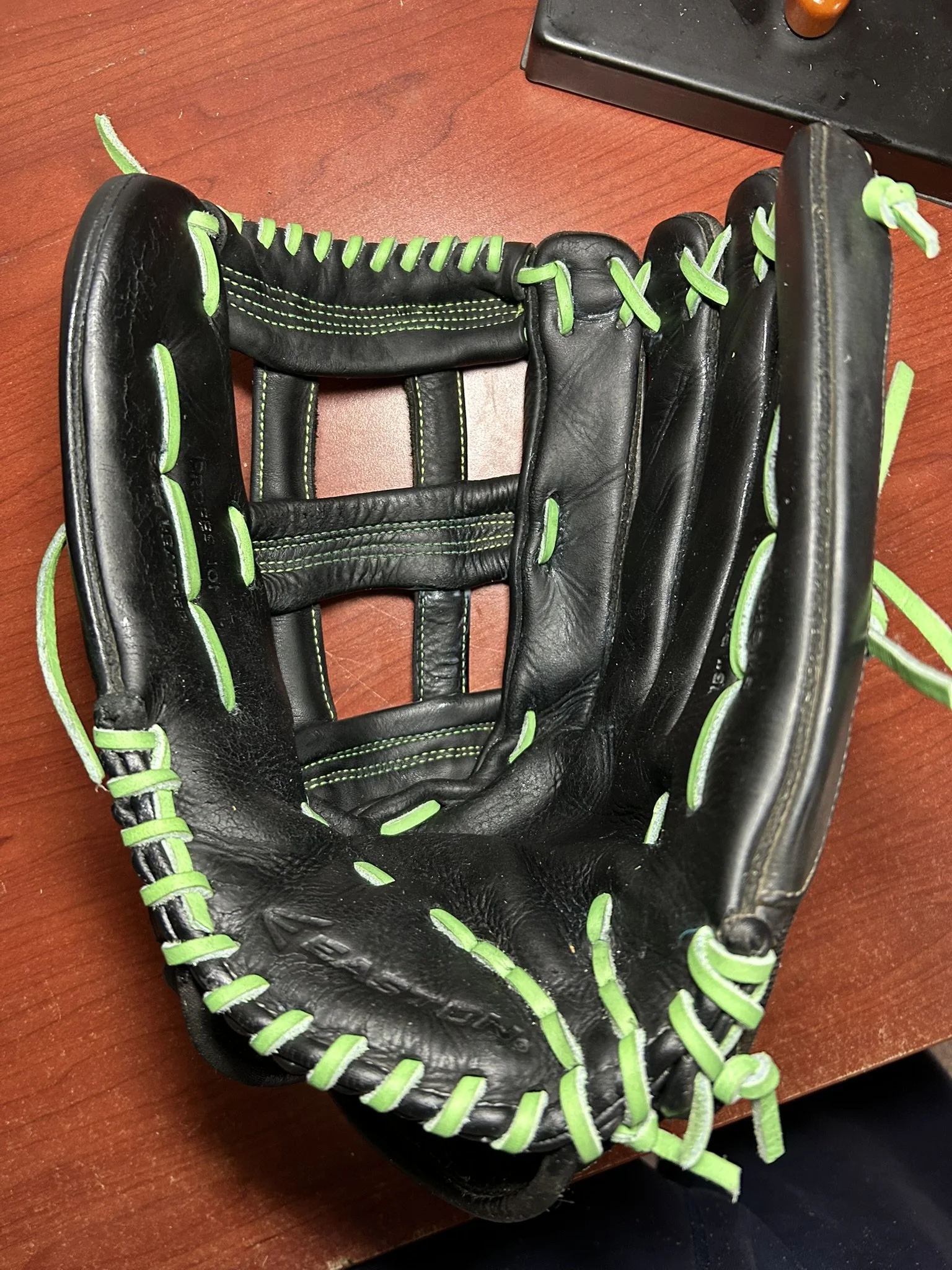 Black baseball glove with green laces resting on a wooden surface.