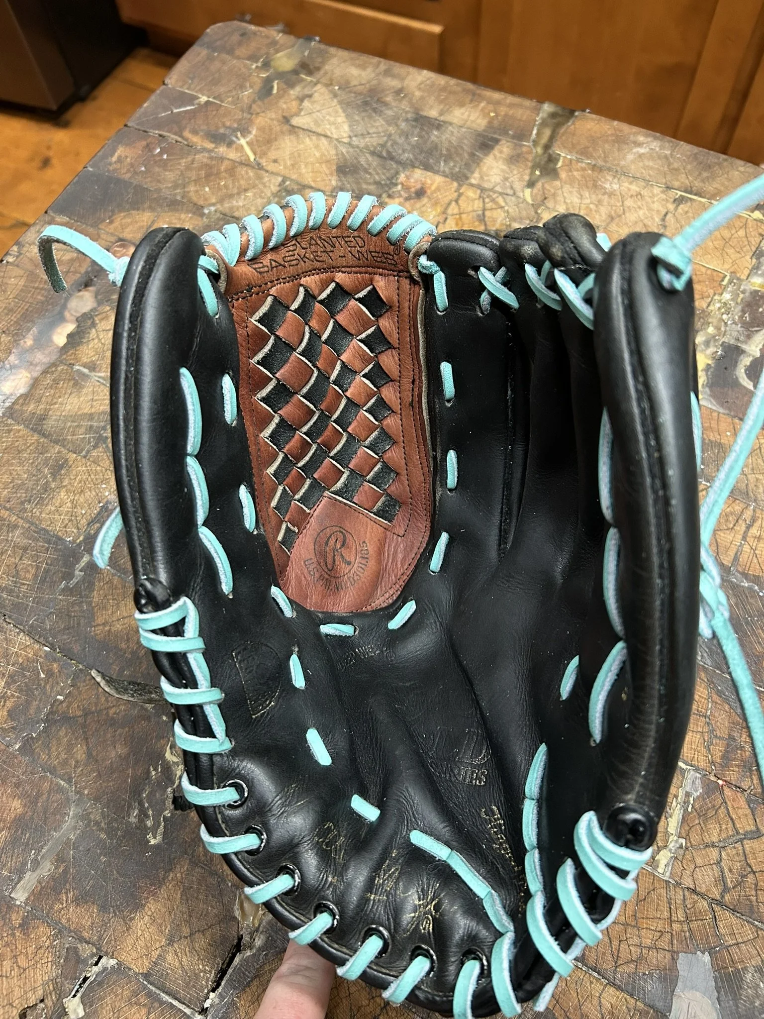 Close-up view of a black and brown baseball glove with blue lacing, resting on a cracked wooden surface.