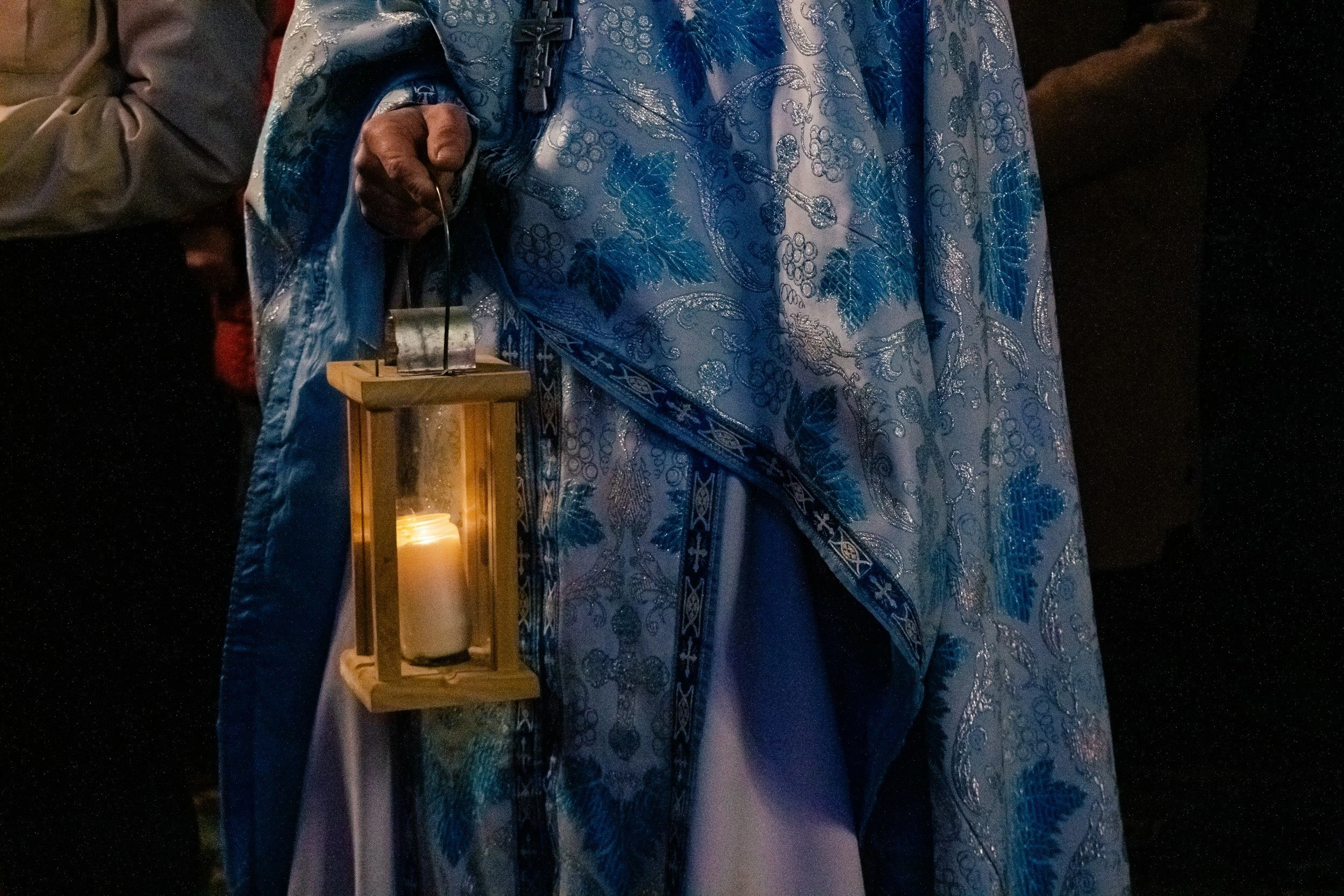 Person wearing a blue and silver patterned robe holding a lantern with a candle inside.
