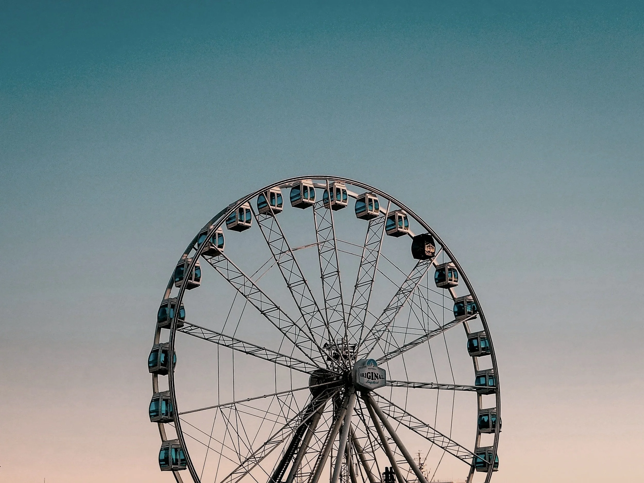A large Ferris wheel with enclosed gondolas against a clear sky at dusk or dawn.