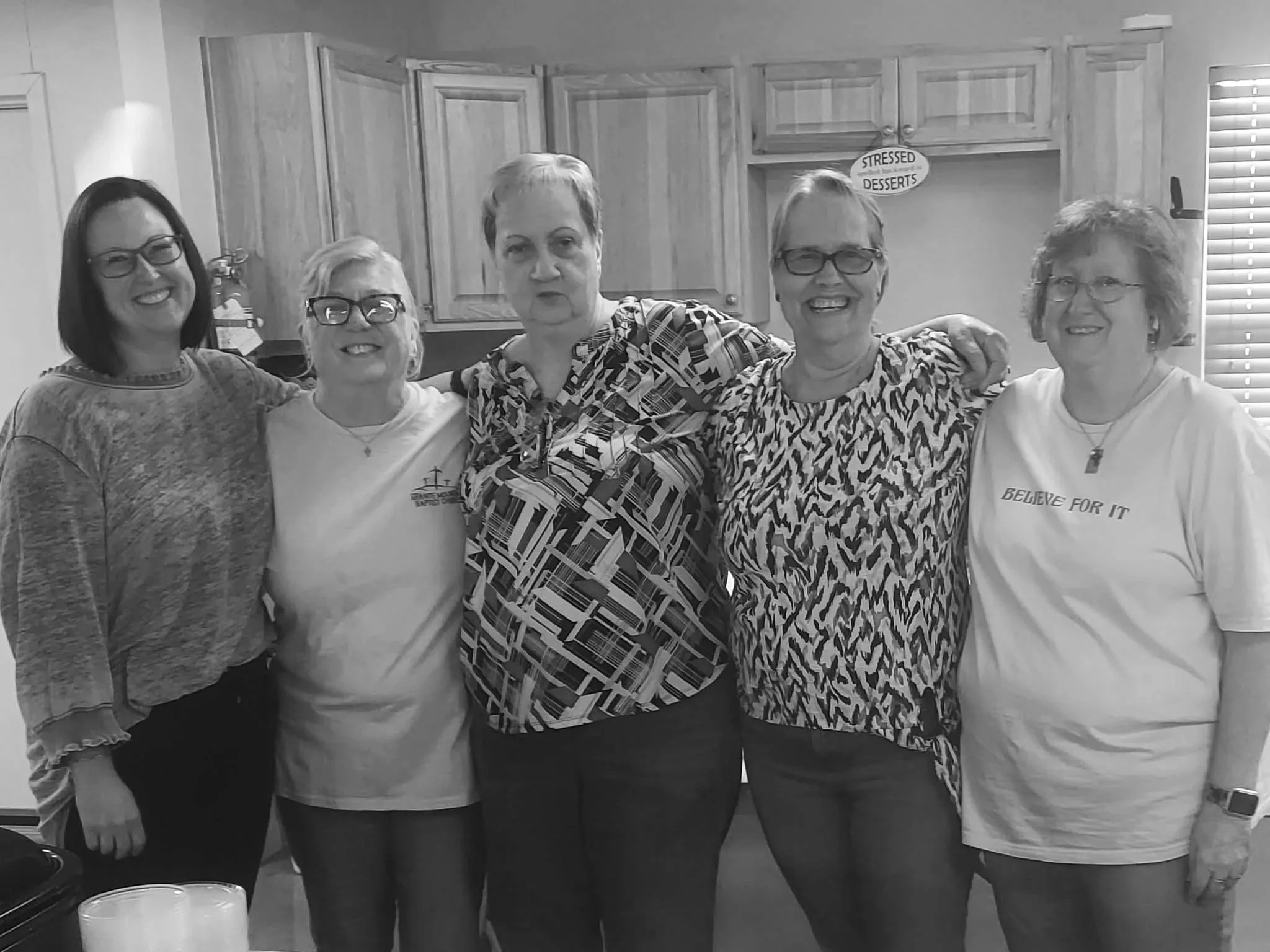 Five women standing together in a kitchen, smiling and posing for a photo.