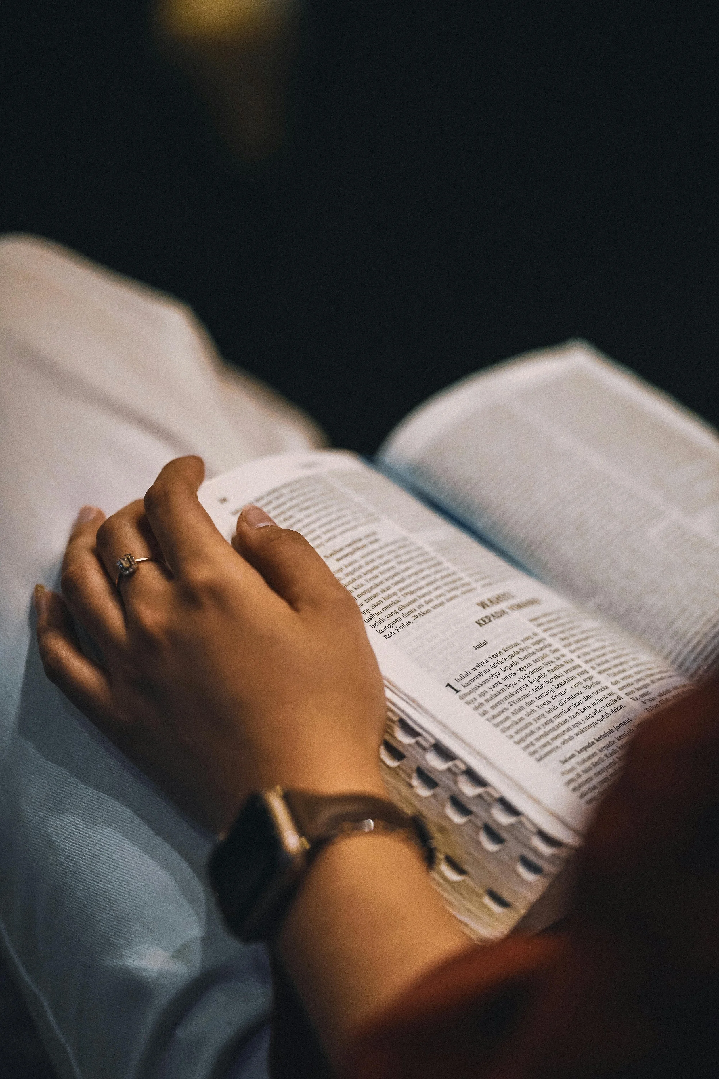 Person reading a Bible or religious book with a wedding ring and watch on their hand.